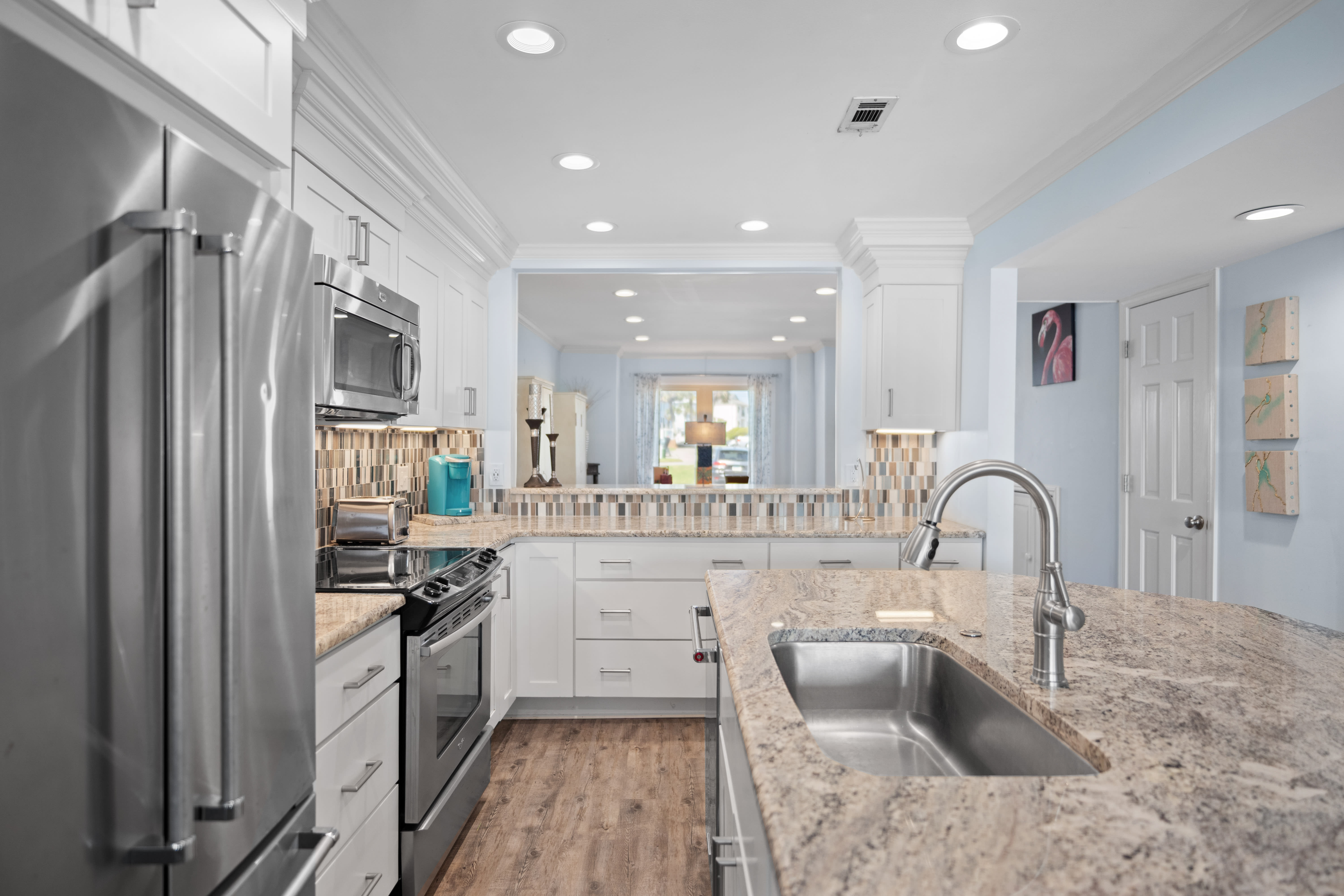 Contemporary kitchen with granite countertops, stainless steel appliances, white cabinetry, and a stylish backsplash. Features an open layout with bar seating.