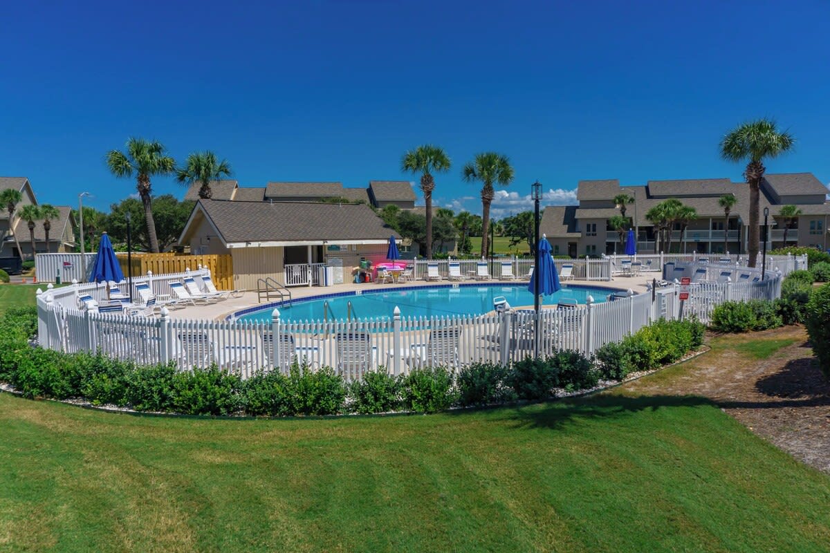 Resort-style pool area with lounge chairs, umbrellas and palm trees, perfect for sunny, relaxing days.