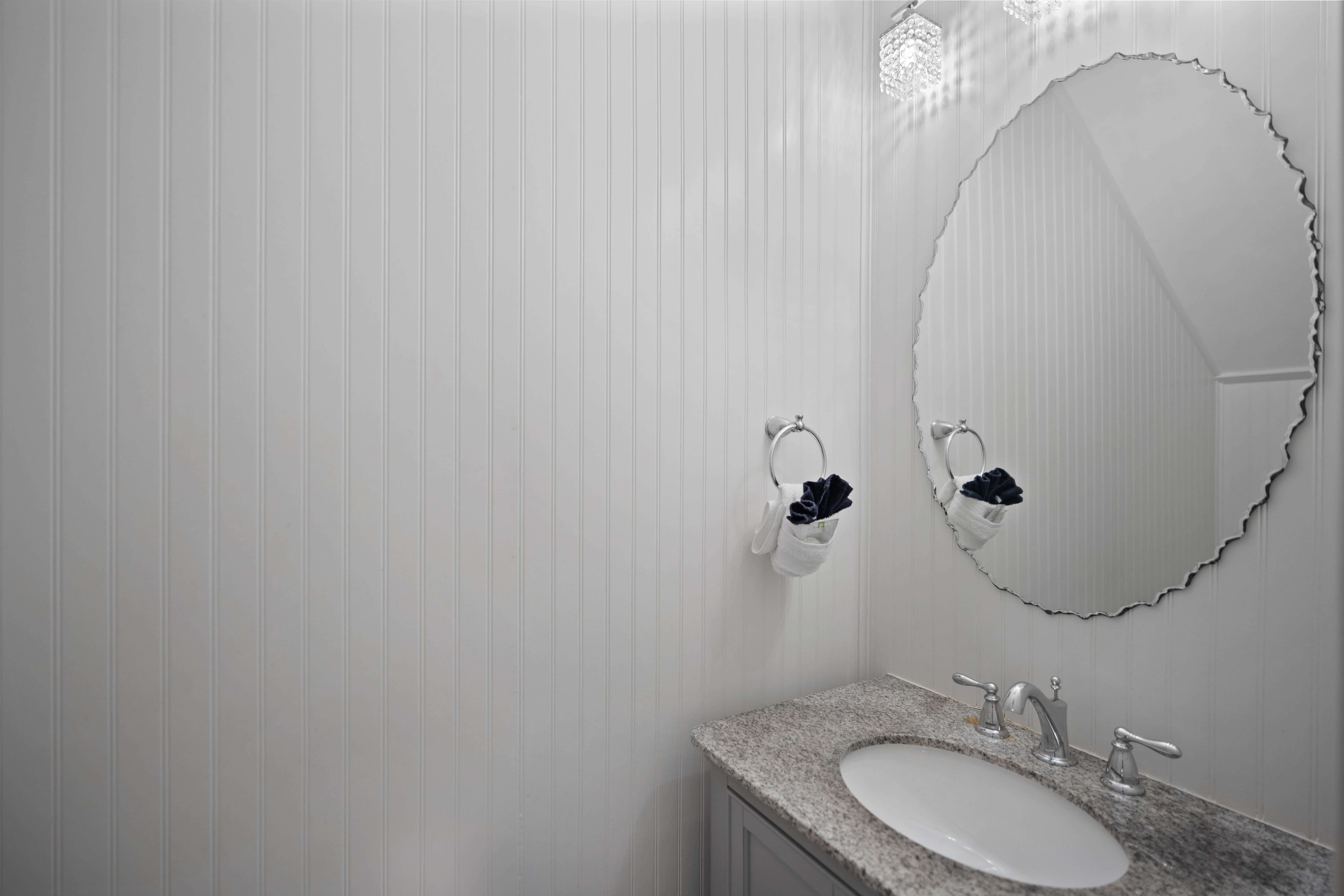 Chic half bathroom with white beadboard walls and a granite countertop. Features sleek chrome fixtures and a modern light fixture for a clean, coastal look.