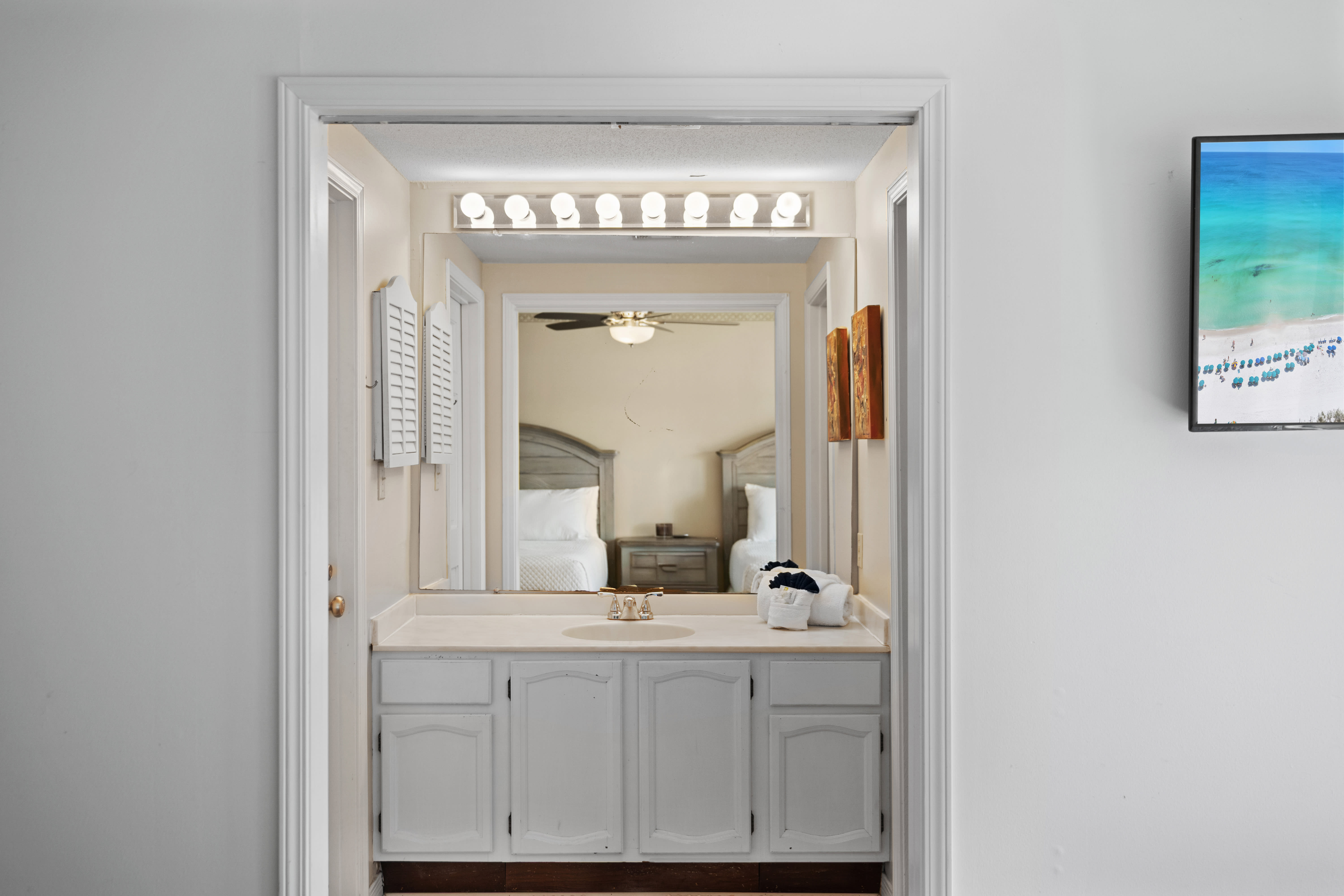 Guest ensuite vanity area with wide countertop, large mirror, bright Hollywood-style lighting, and white cabinetry. Clean and functional, with direct access to the bedroom.