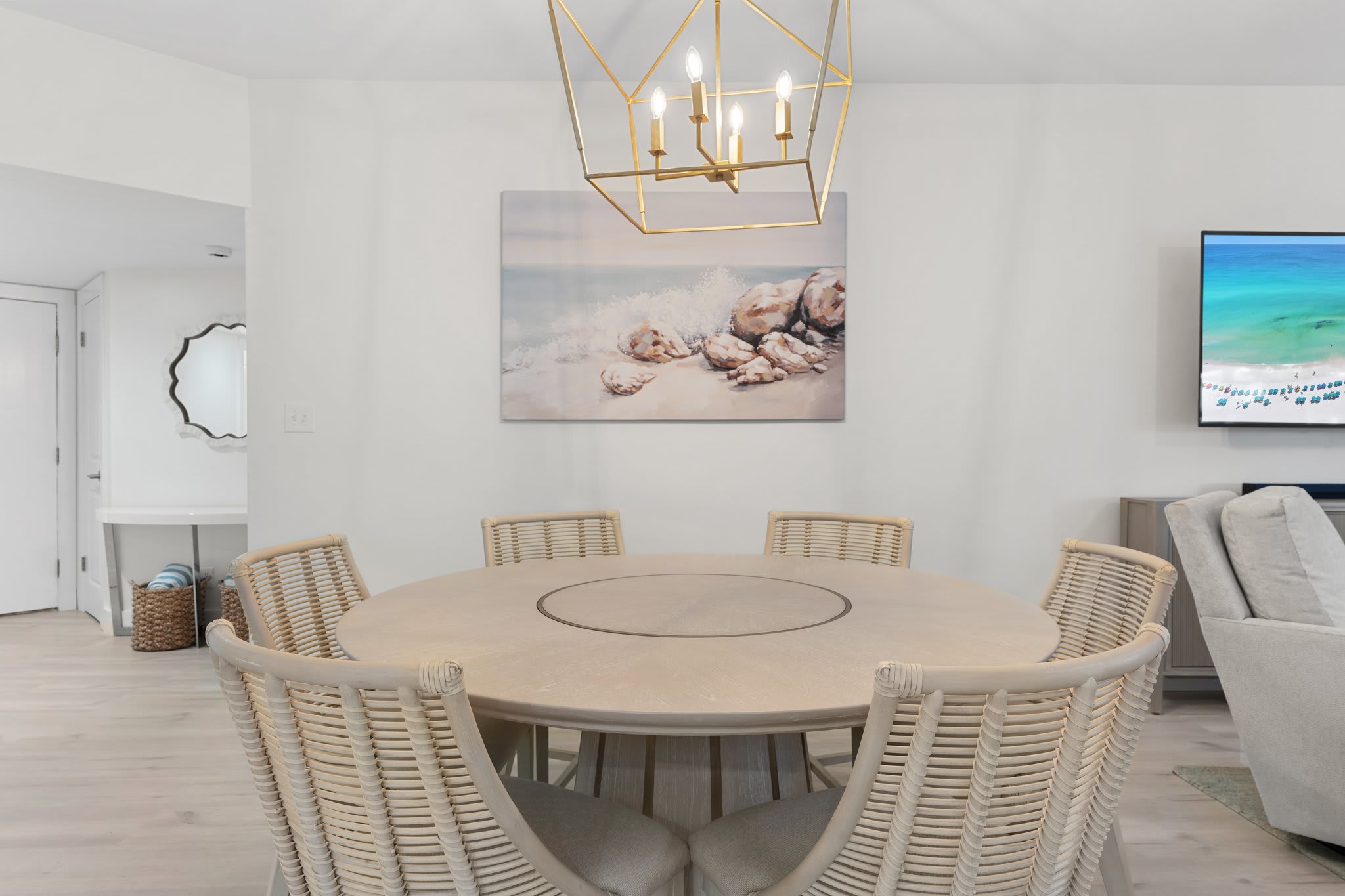 Gather in this coastal-chic dining space featuring a round wood table, woven chairs, and elegant lighting.