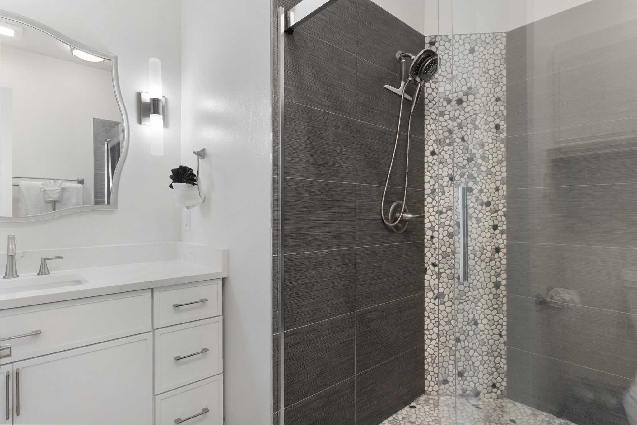 The en-suite bathroom showcases a custom walk-in shower with dark tile, pebble accents, and modern finishes.