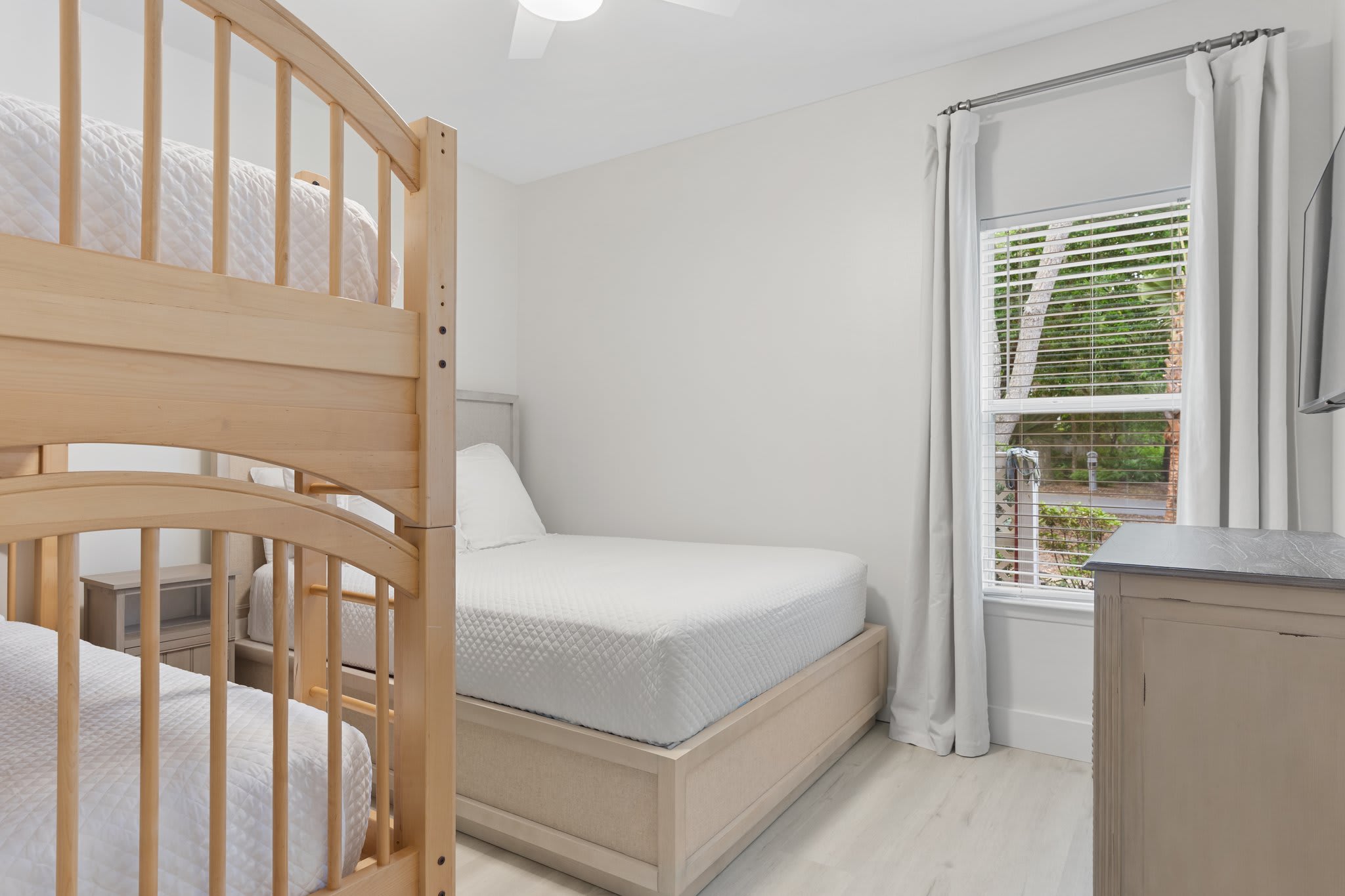 This light-filled guest room offers a queen bed and twin bunks, creating a perfect space for family comfort.