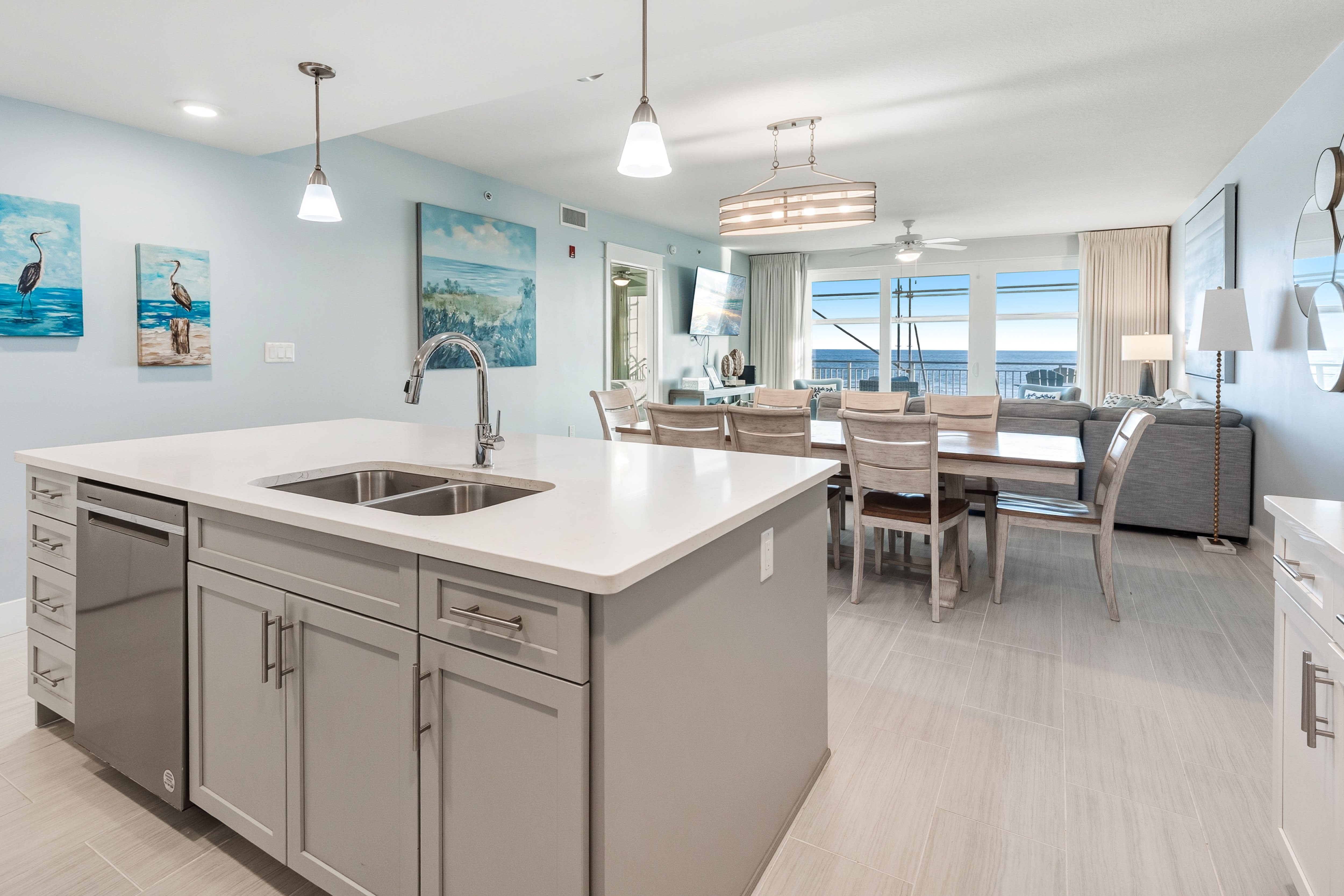 Your open-concept kitchen flows seamlessly into the dining area, where ocean views frame every meal and coastal artwork completes the beachside ambiance.