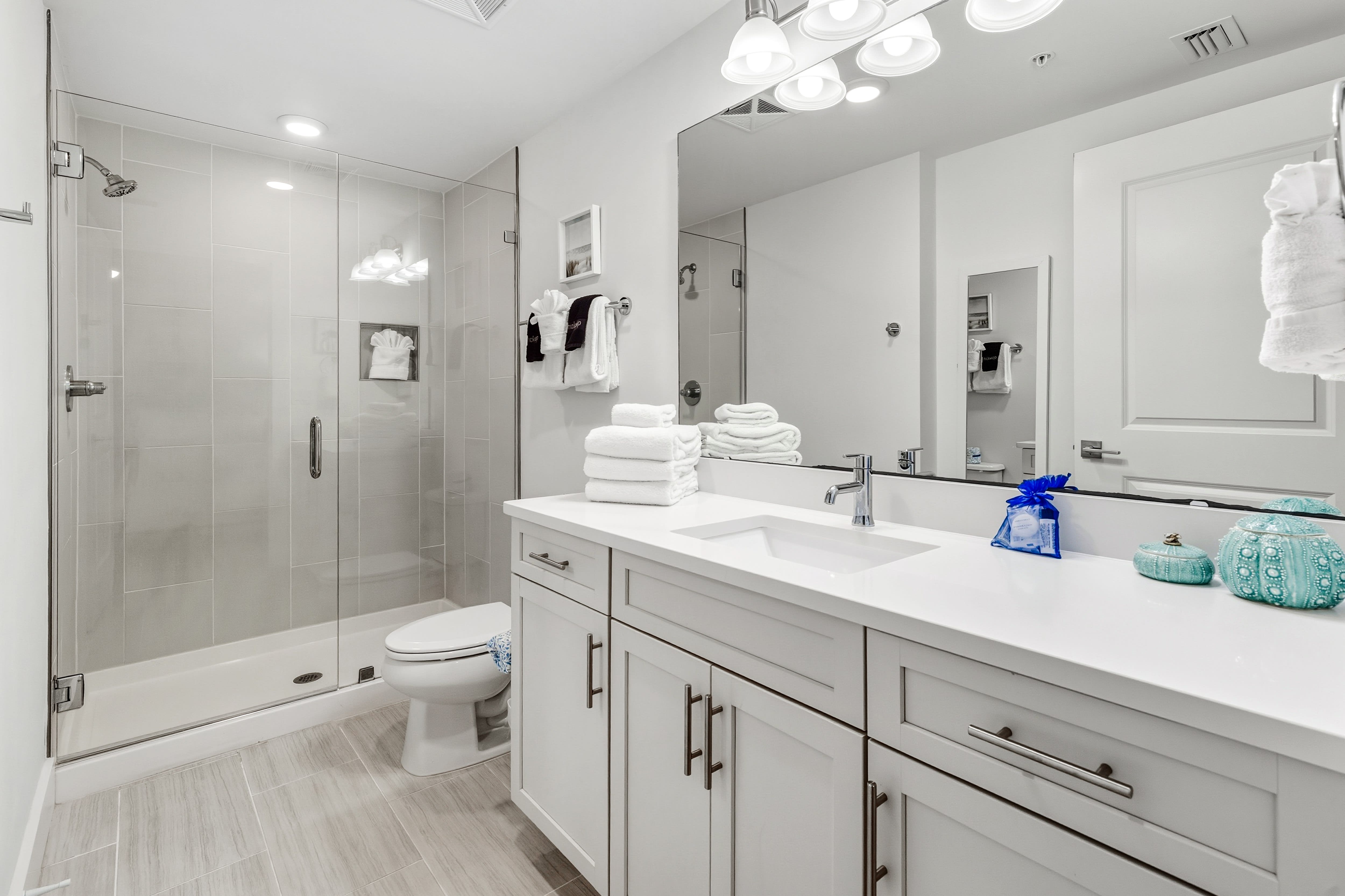 Step into your serene spa-like bathroom with gleaming white surfaces, a spacious glass shower, and fluffy towels waiting for your arrival.