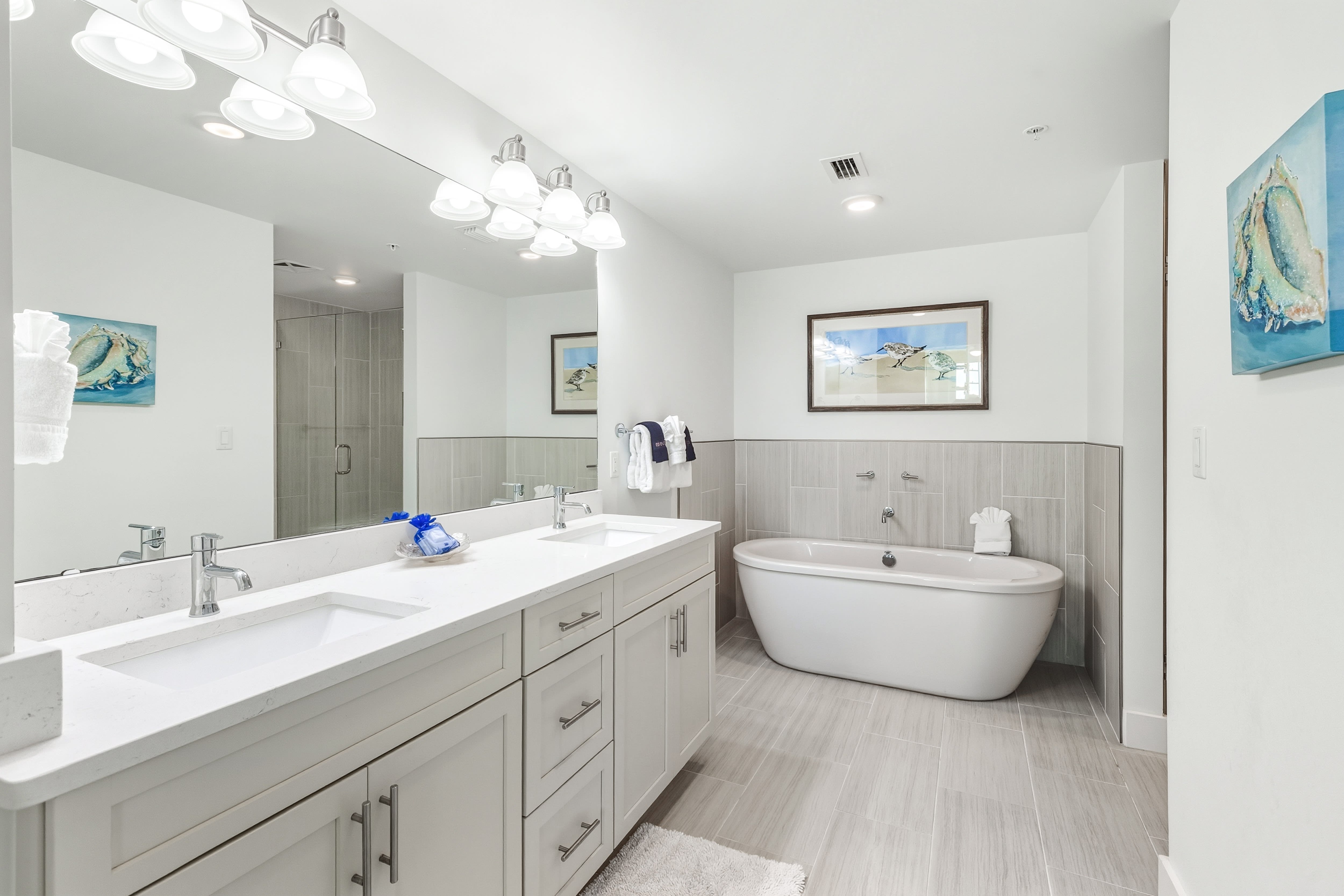 Unwind in your spa-like bathroom featuring a luxurious soaking tub, dual vanities, and elegant coastal artwork.