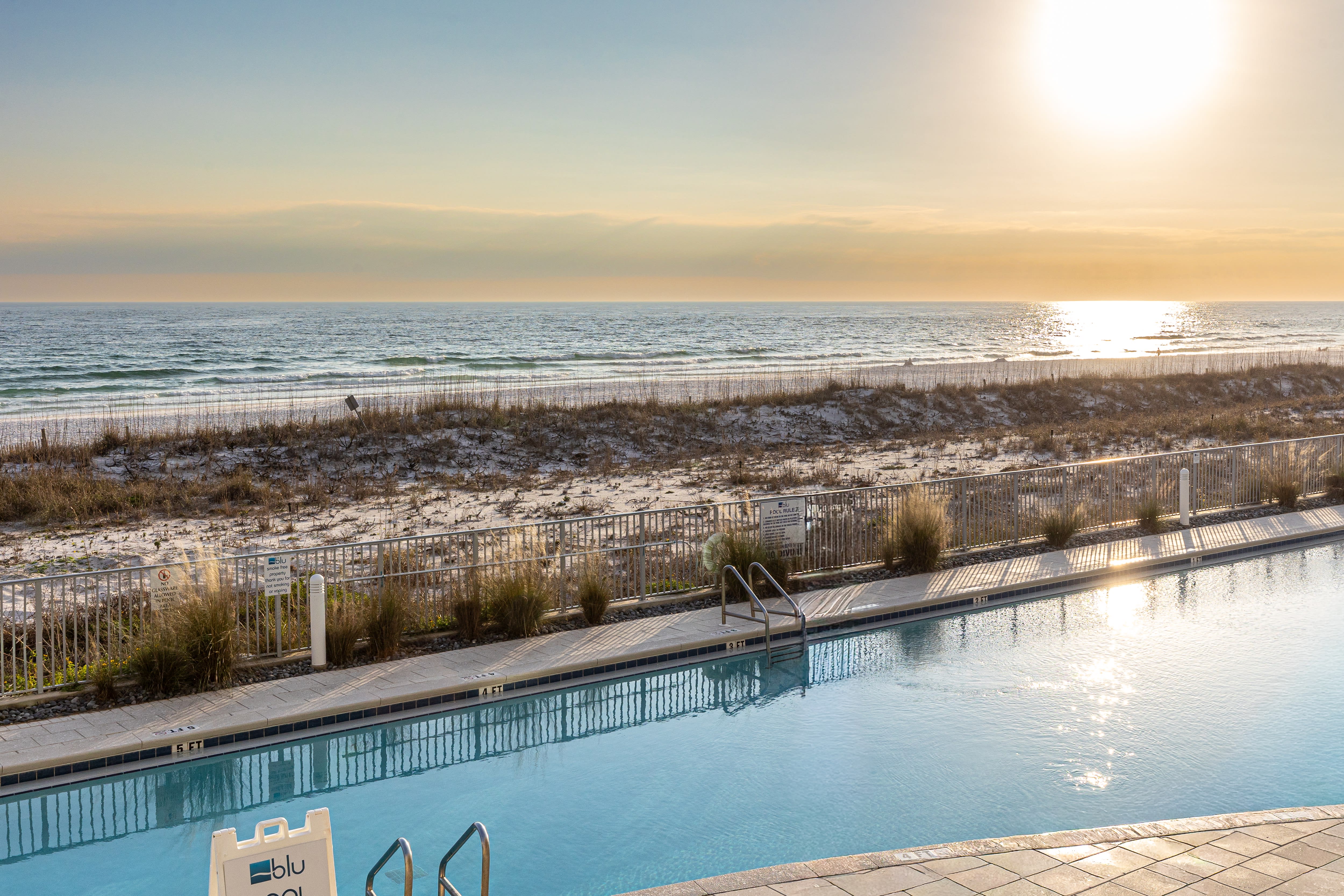 Beachfront swimming pool overlooking pristine sandy shores and ocean waves at sunset.