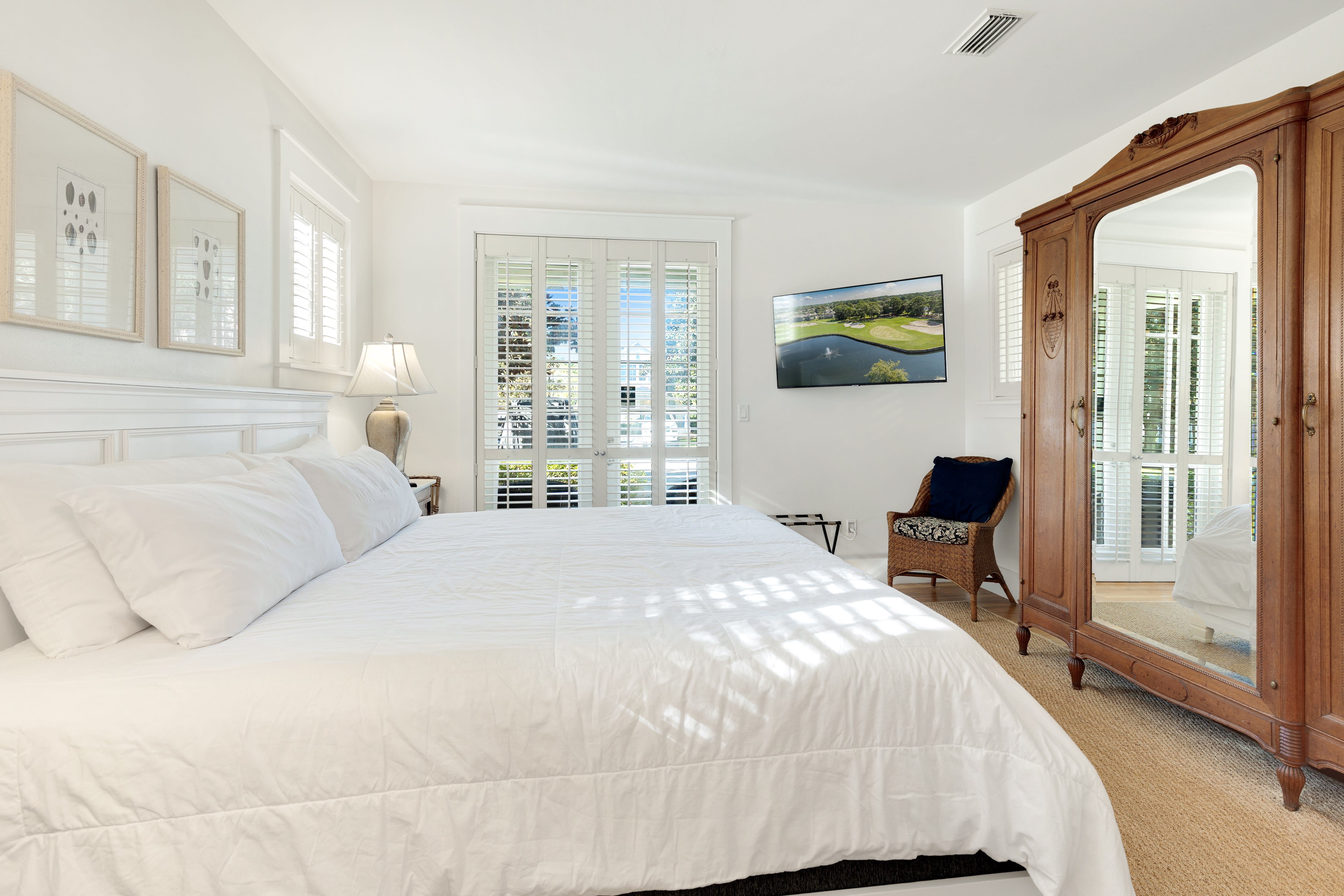Drift off in your serene bedroom with crisp white linens, elegant plantation shutters, and an antique armoire creating the perfect coastal retreat.
