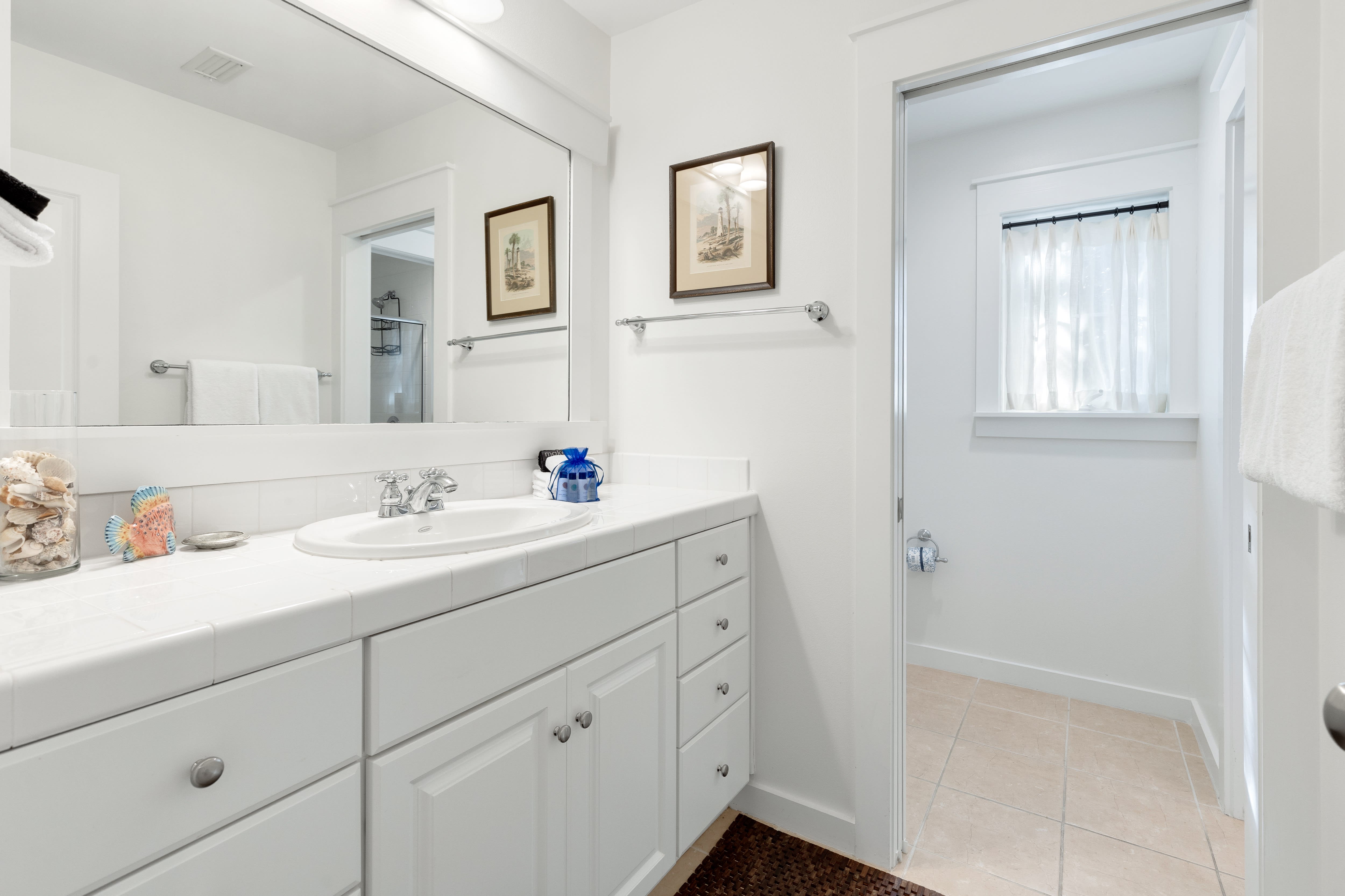 Step into your pristine bathroom featuring crisp white cabinetry, spacious vanity, and charming nautical artwork that creates a serene coastal atmosphere.