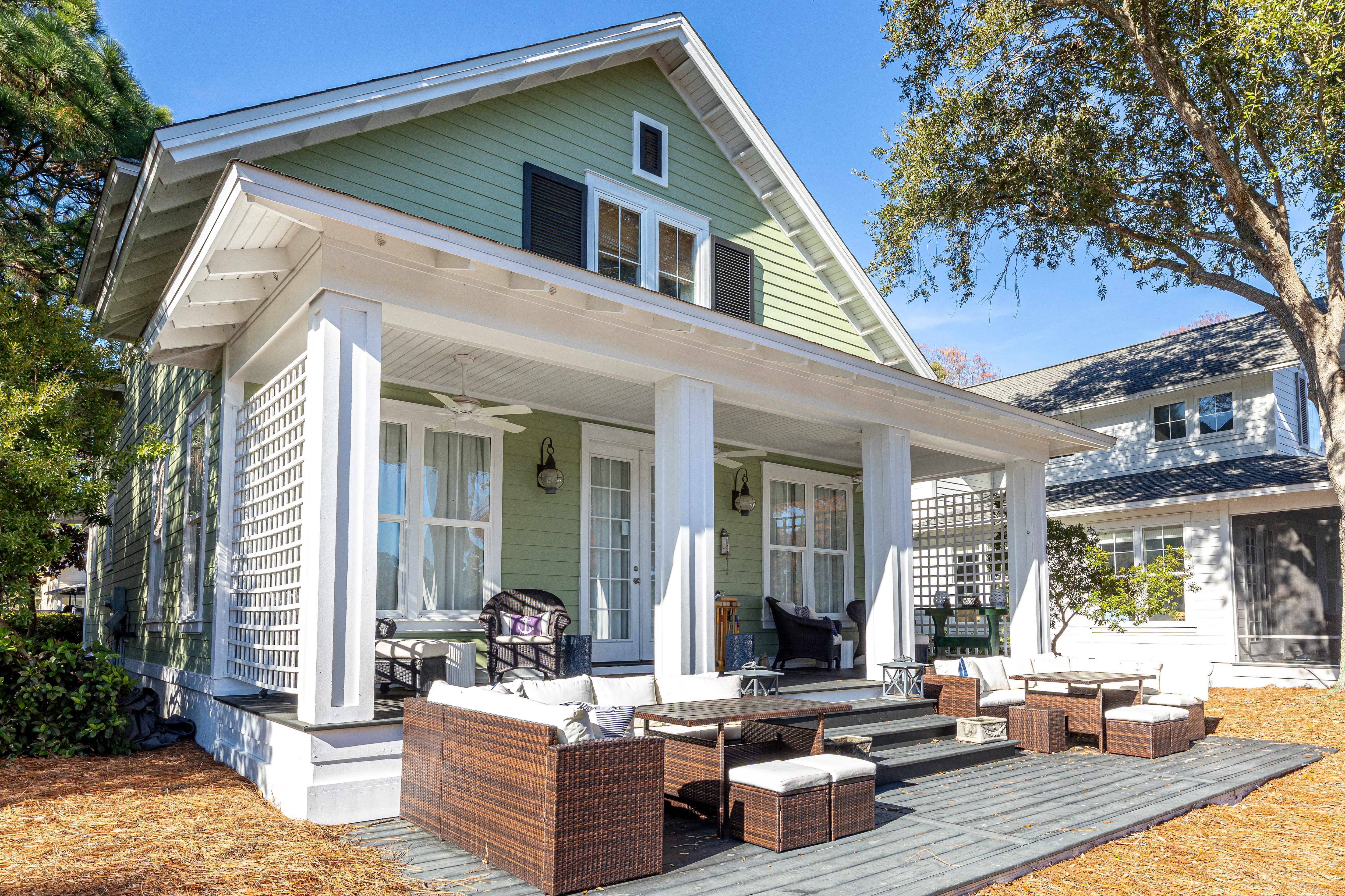 Charming green cottage with spacious covered porch featuring comfortable outdoor furniture for relaxing in the fresh air.