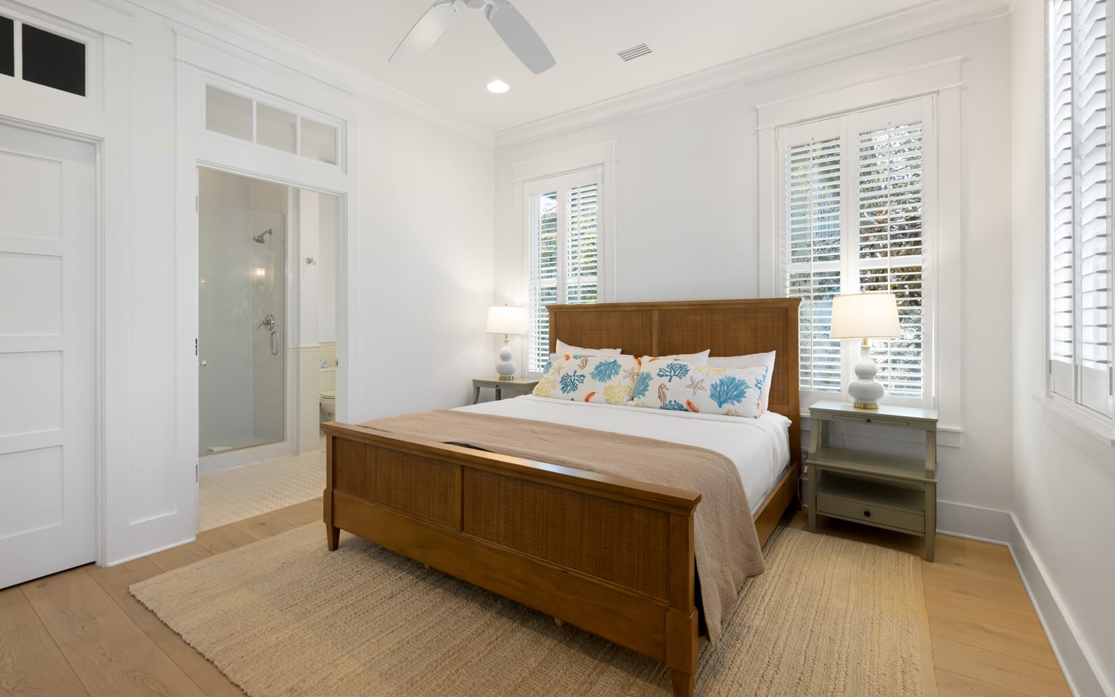 Your bright bedroom features warm wood furnishings and coastal-inspired linens, with natural light streaming through plantation shutters for peaceful mornings.