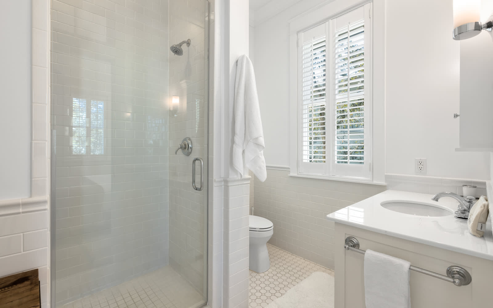 Step into your private spa-like bathroom with a luxurious glass shower, pristine white fixtures, and natural light streaming through plantation shutters.