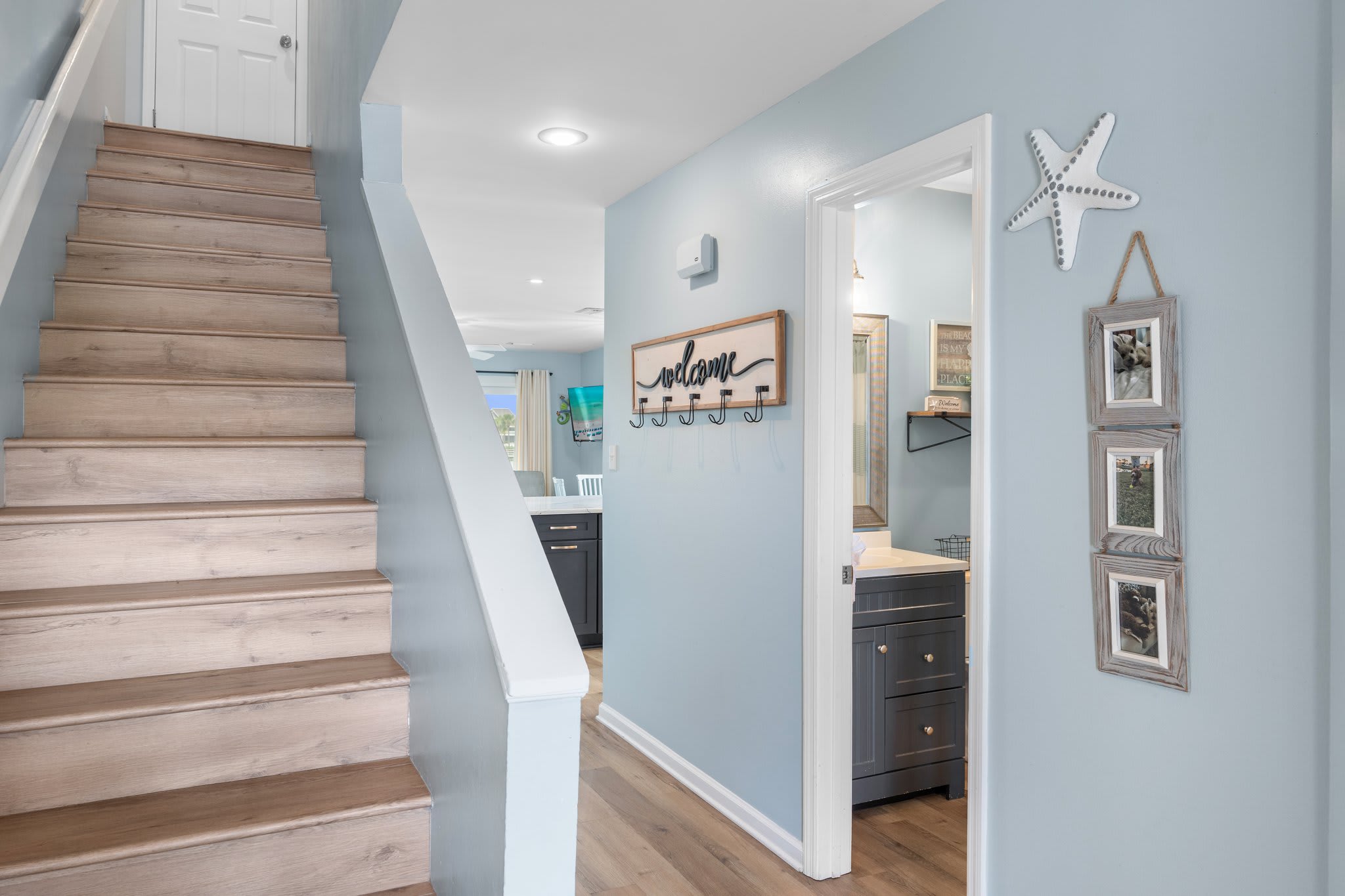 Charming entry hallway with beachy décor leads to a full bath and staircase, offering a warm welcome into this stylish coastal retreat.
