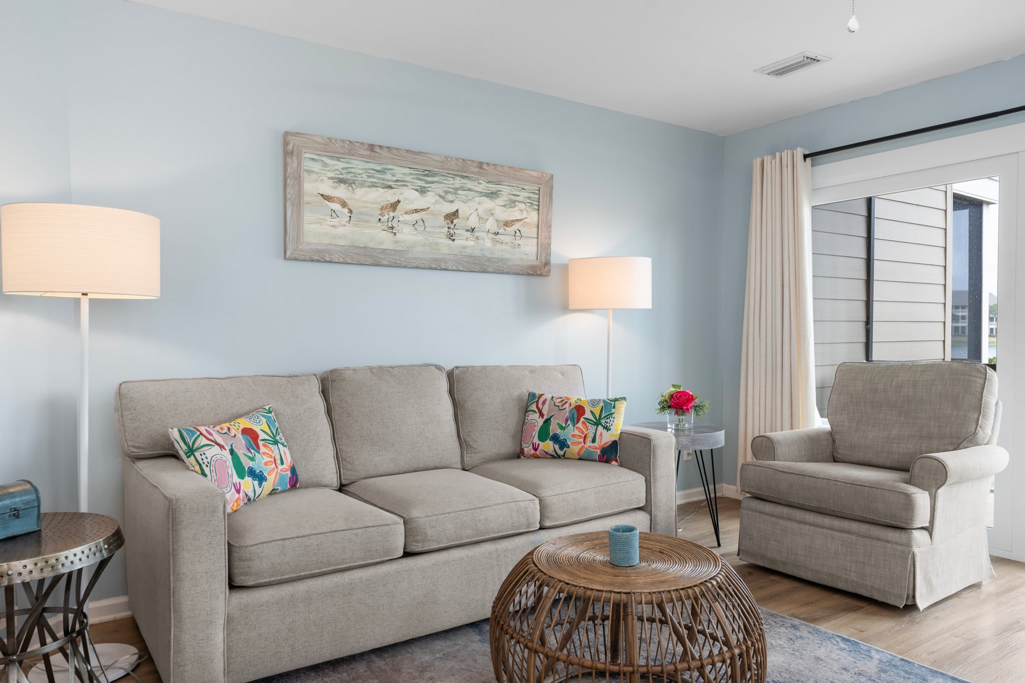 Cozy coastal living room with a plush sofa, tropical accent pillows, rattan coffee table, and beach-themed wall art—perfect for relaxing after a day in the sun.