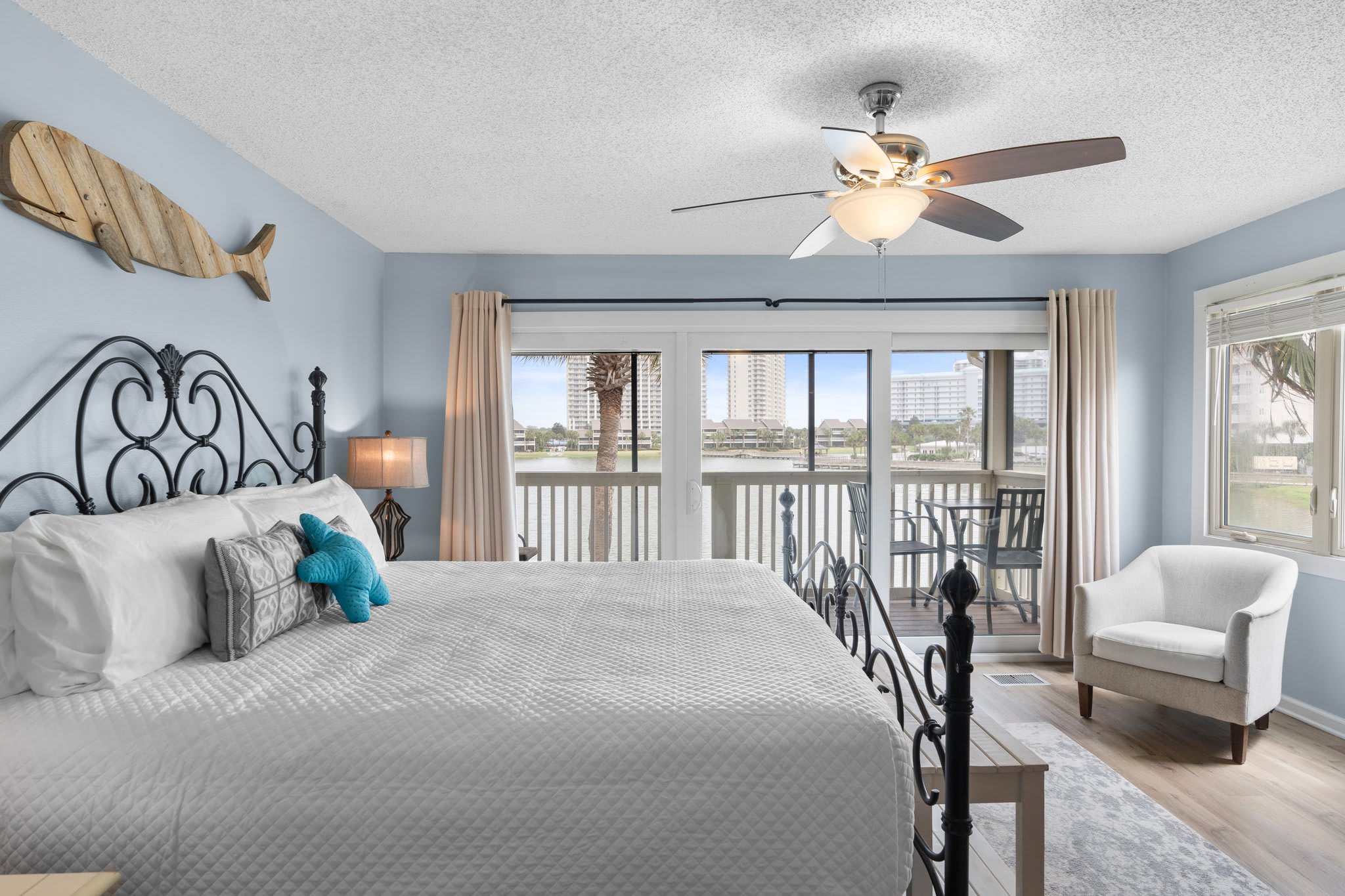 Wake up to stunning lake views in the airy primary bedroom featuring a plush king bed, soft coastal tones, and direct access to a private balcony for peaceful mornings or sunset unwinding.