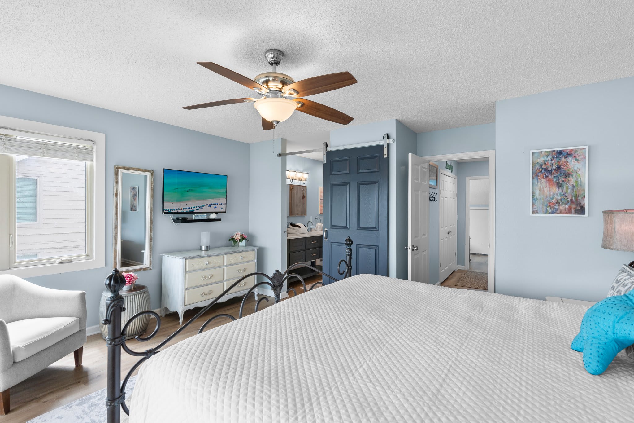 Primary bedroom features a king bed, wide-screen TV, and en-suite bath with a stylish barn door—combining comfort, privacy, and coastal charm in one relaxing space.