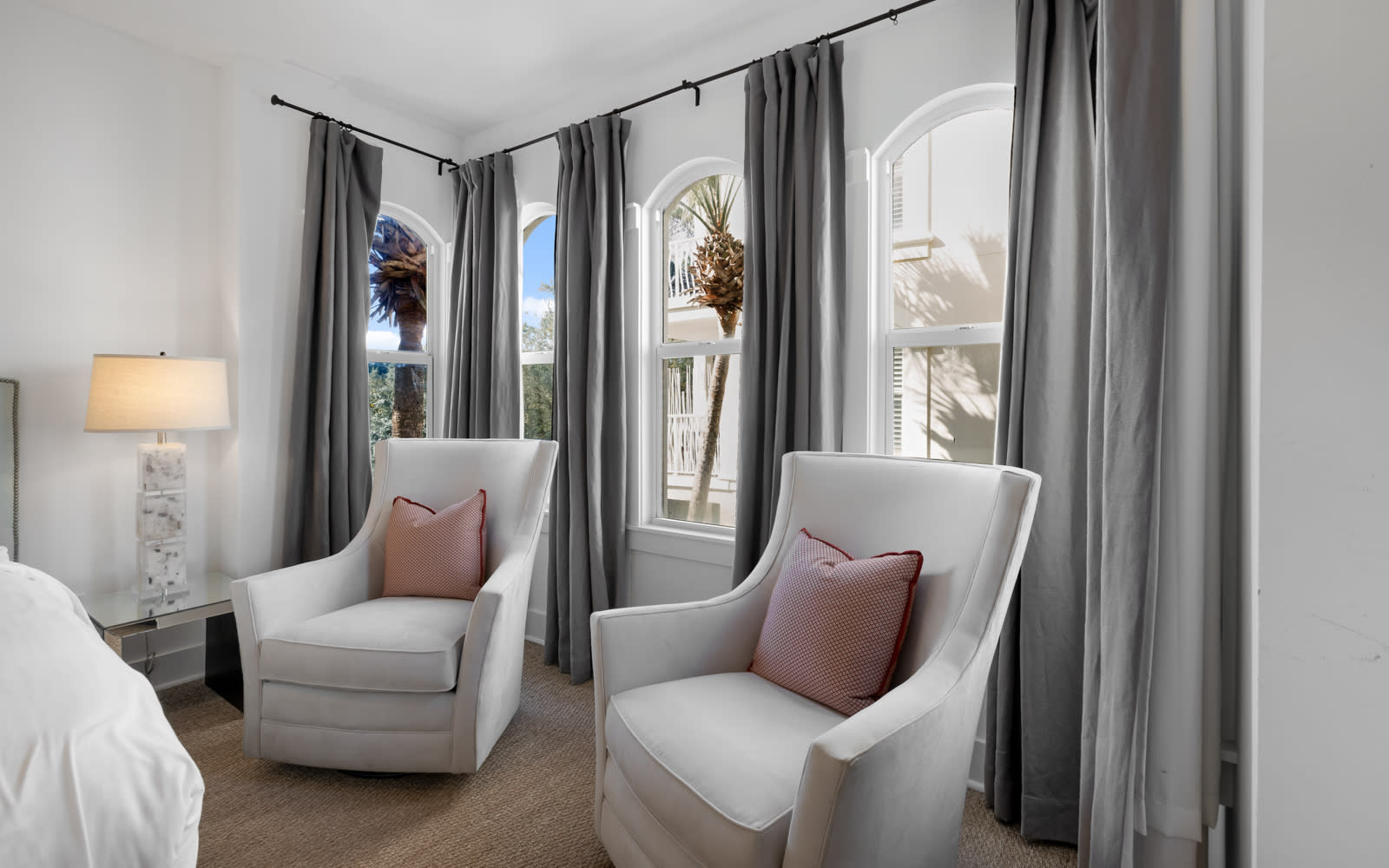 Sink into plush armchairs by graceful arched windows, where soft gray curtains frame palm-dotted views and morning light creates your perfect reading retreat.
