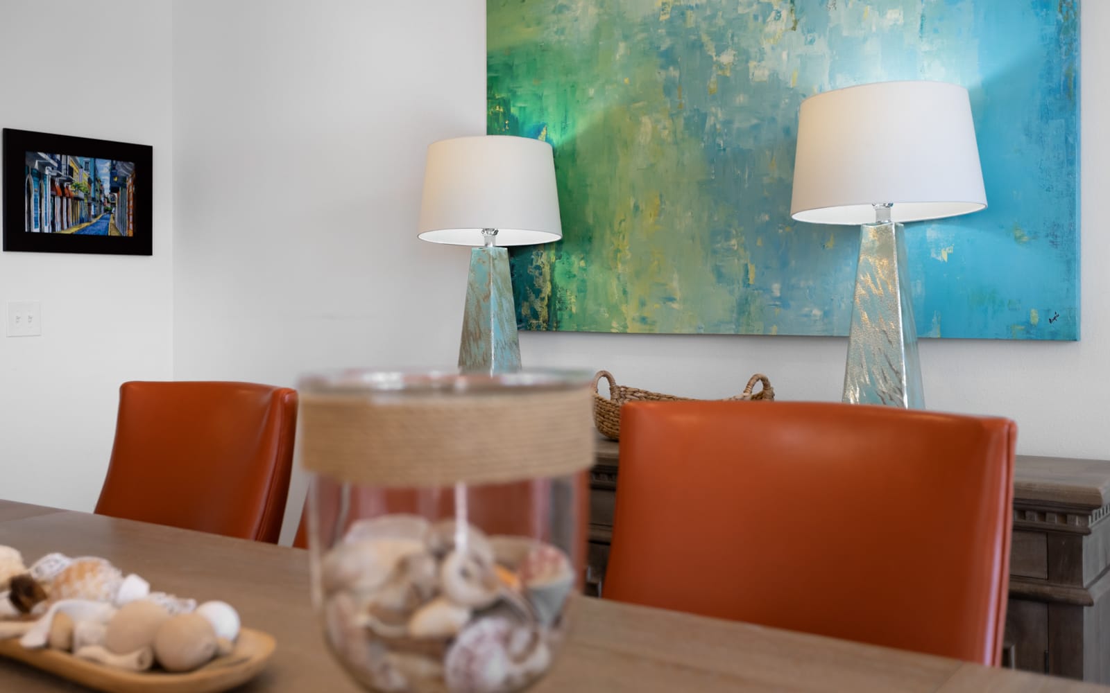 Gather around this stylish dining table where warm orange chairs and ocean-inspired artwork create the perfect setting for your memorable meals.