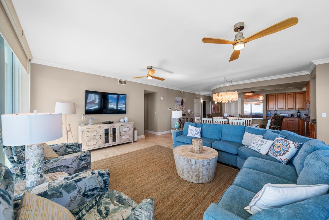 Unwind in your spacious living area where coastal blues meet comfort—plush seating, entertainment center, and ceiling fans create the perfect retreat.