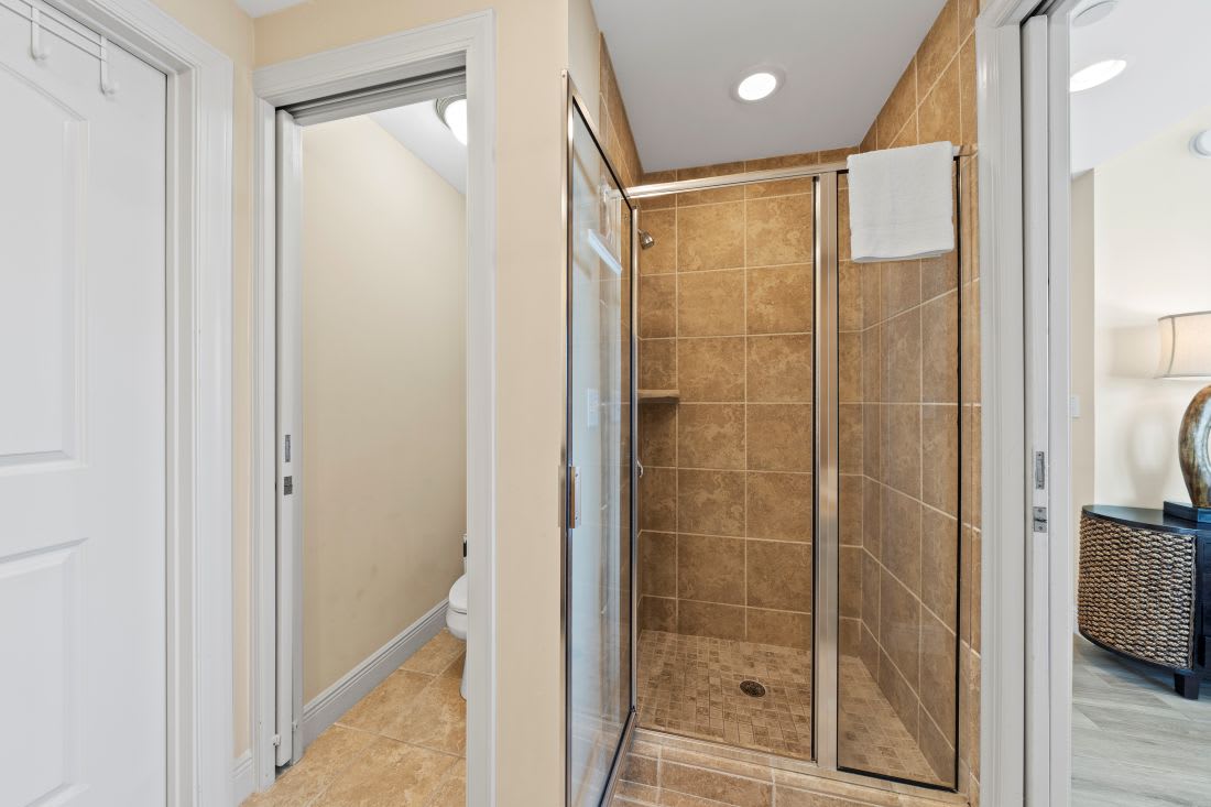 Step into your private spa-like shower featuring beautiful warm stone tile and sleek glass doors for the perfect refreshing escape.