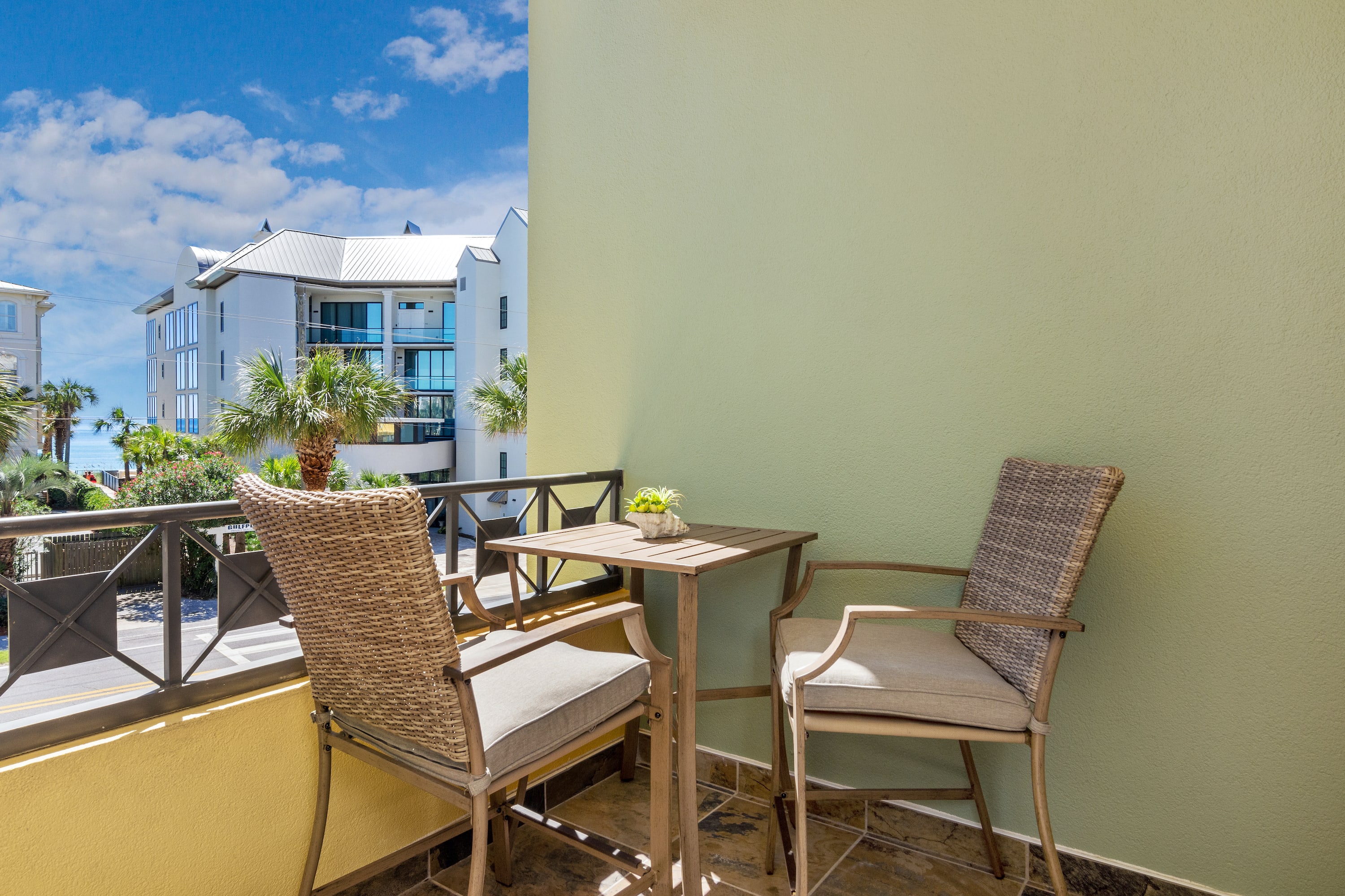 Cozy private balcony with bistro seating and palm-lined views—perfect for morning coffee or evening drinks on 30A.