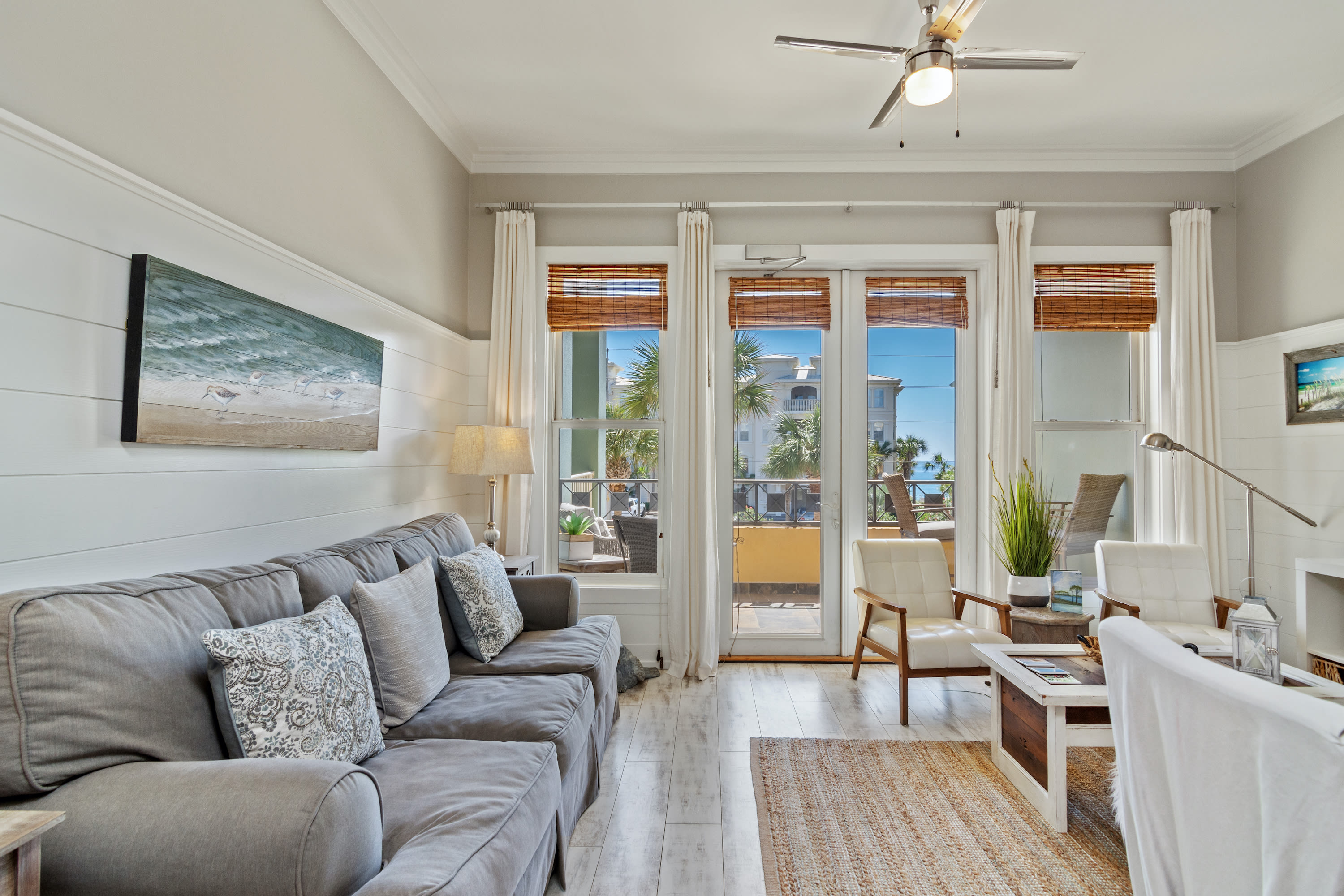 Cozy 30A living space with plush seating, beachy décor, and sunlit French doors leading to a balcony with tropical views—perfect for laid-back coastal living.