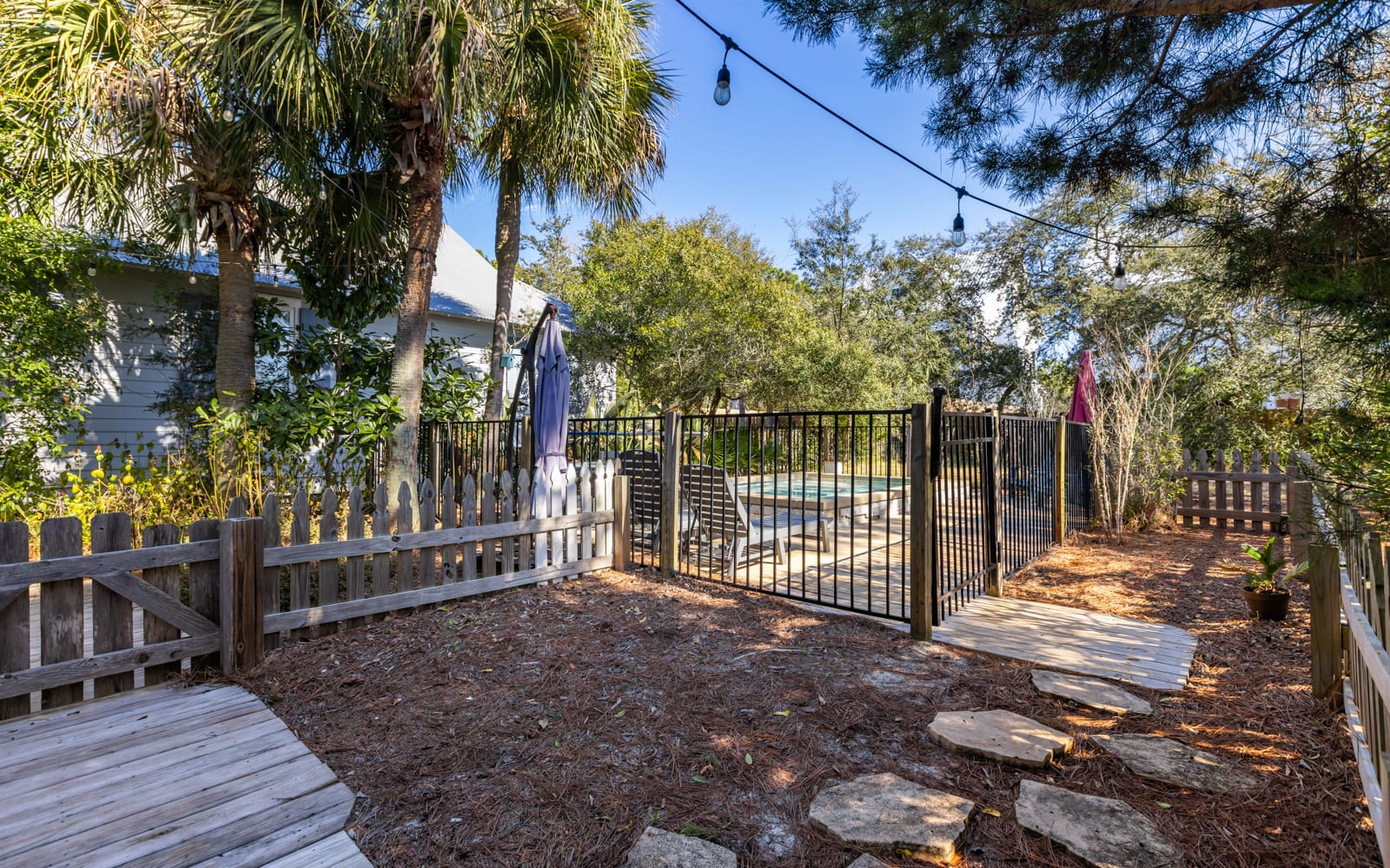 Private backyard oasis with pool access, palm trees, and cozy string lights for evening relaxation.