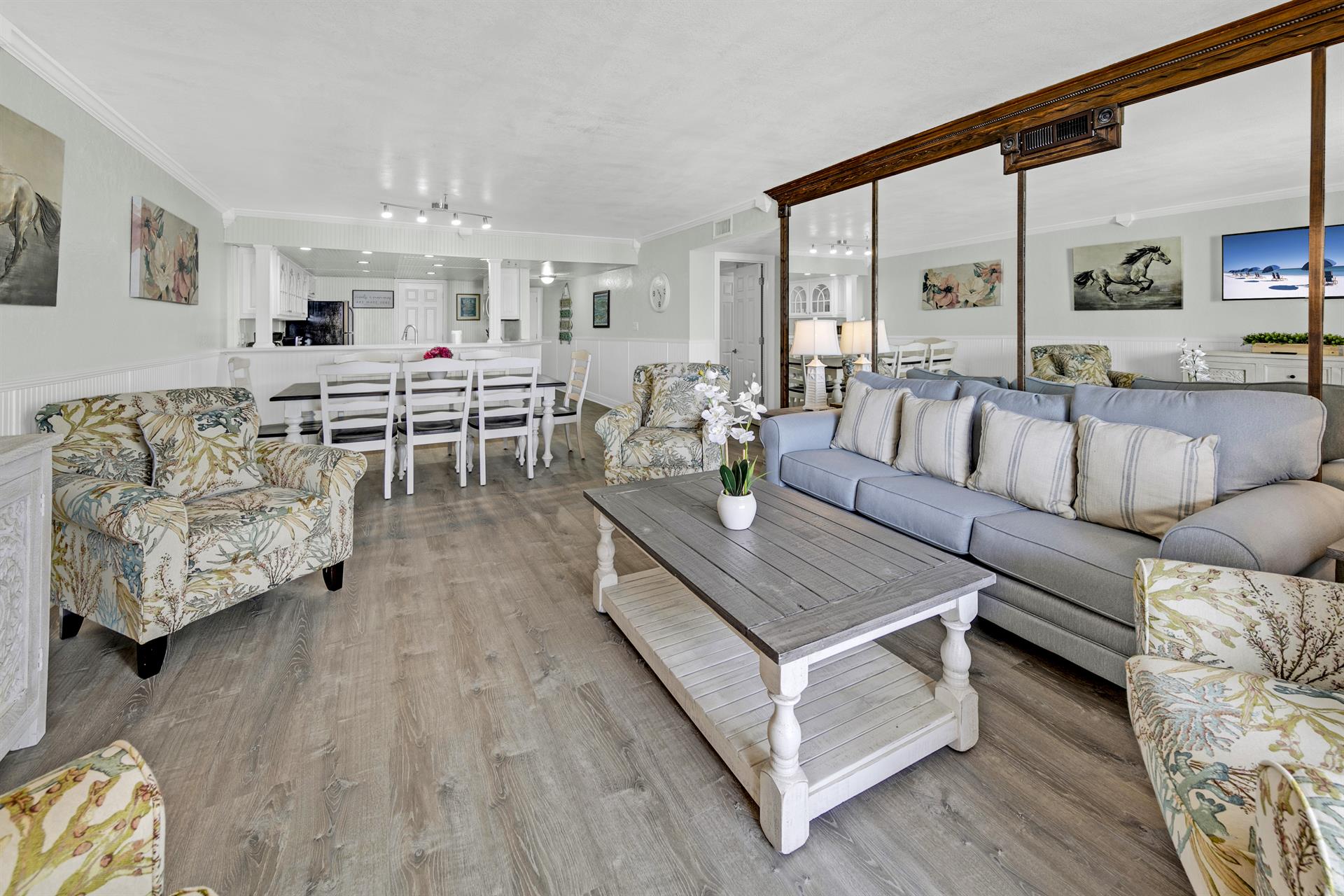 Relax in your spacious living area with comfortable coastal seating, open kitchen access, and charming equestrian artwork creating a welcoming home-away-from-home atmosphere.