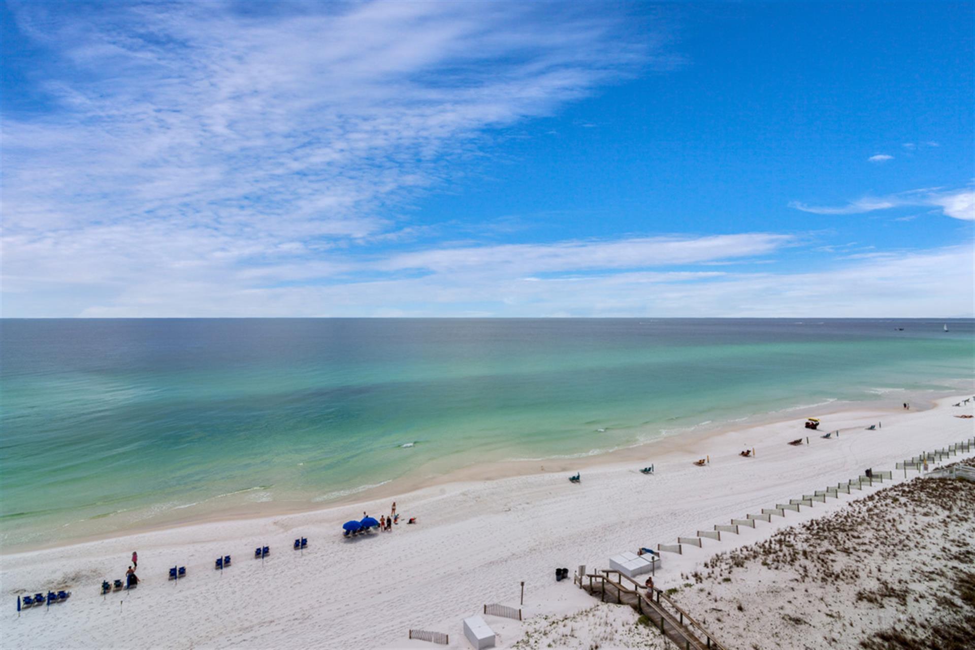 Pristine white sand beach stretches along emerald waters under brilliant blue skies dotted with wispy clouds.