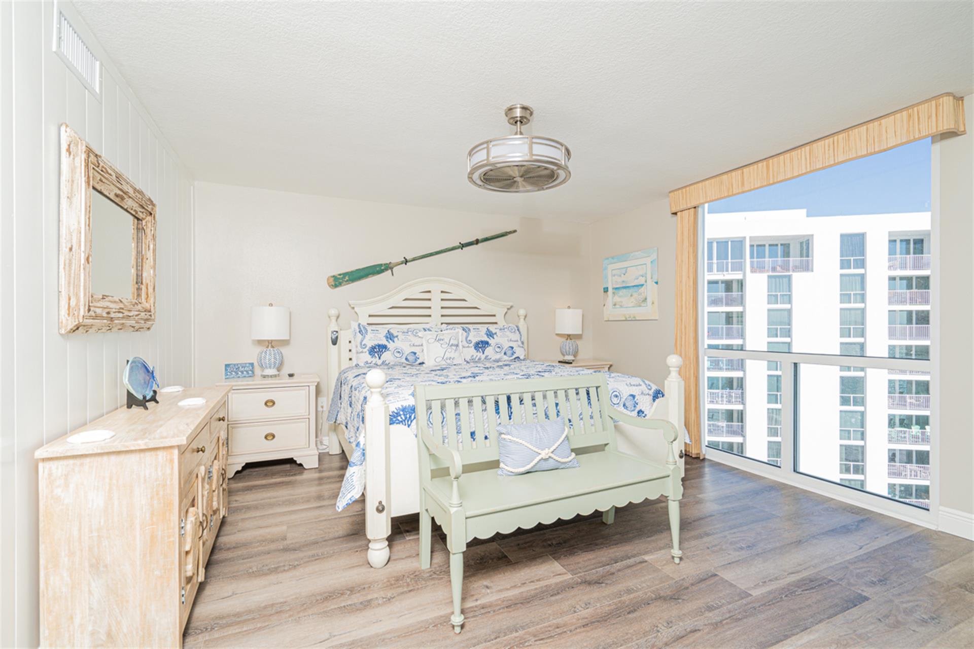 Your coastal bedroom features nautical charm with ocean-inspired bedding and expansive city views through floor-to-ceiling windows.