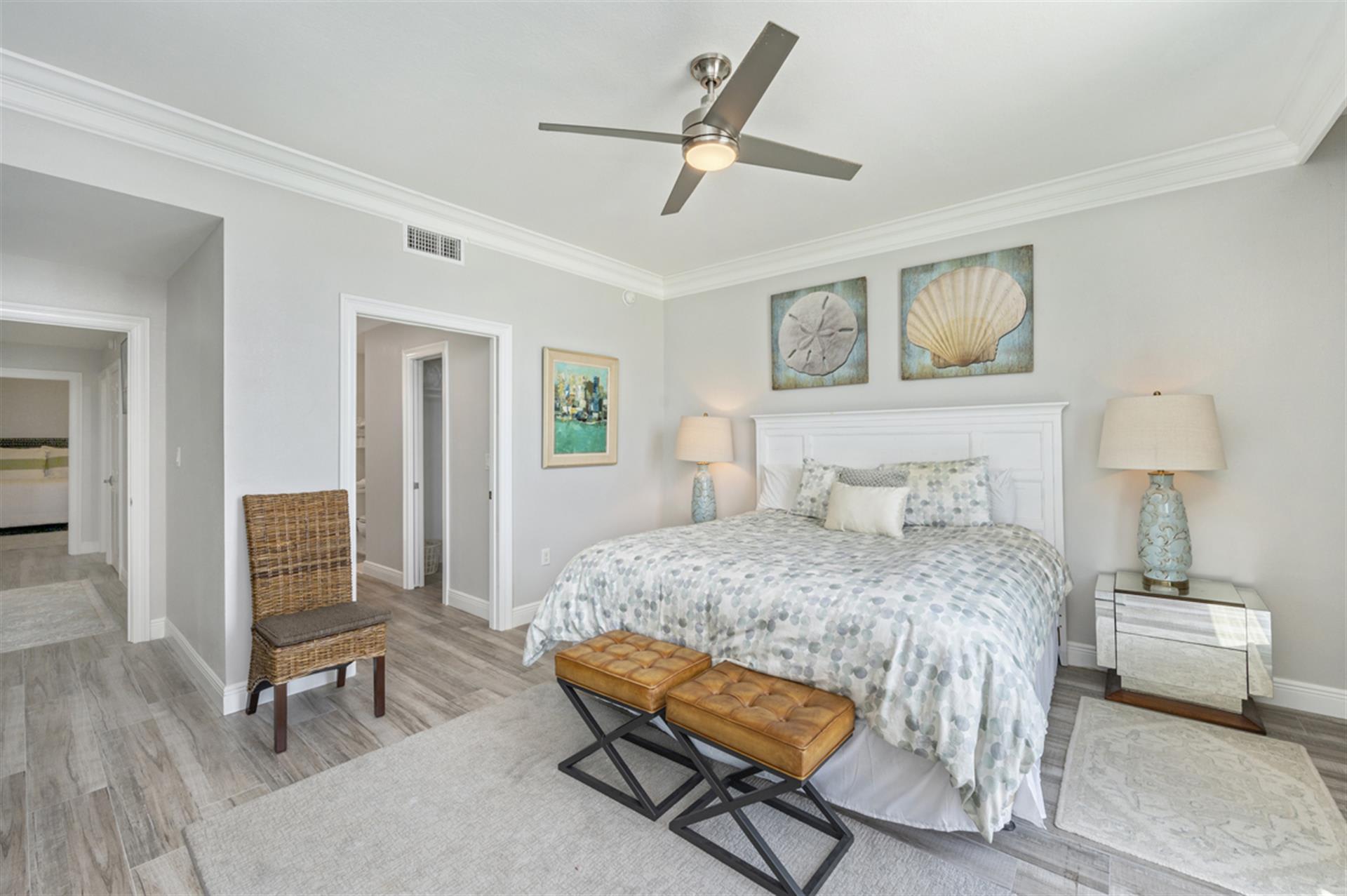 Relax in your coastal-inspired bedroom with ocean artwork, soft lighting, and a ceiling fan for comfort.