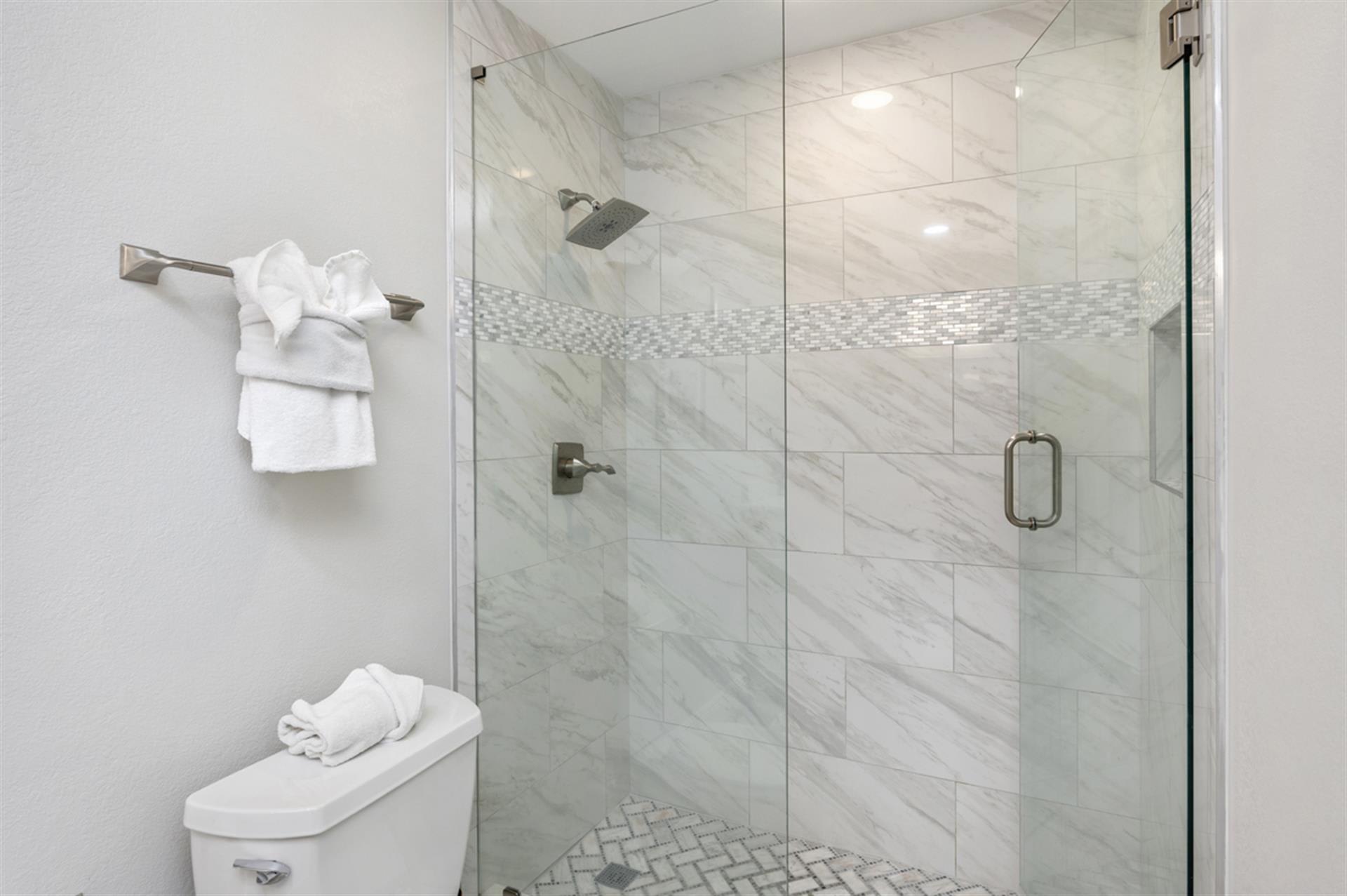 Step into your luxurious marble-clad shower with rainfall head and mosaic accents. Fresh towels await nearby.