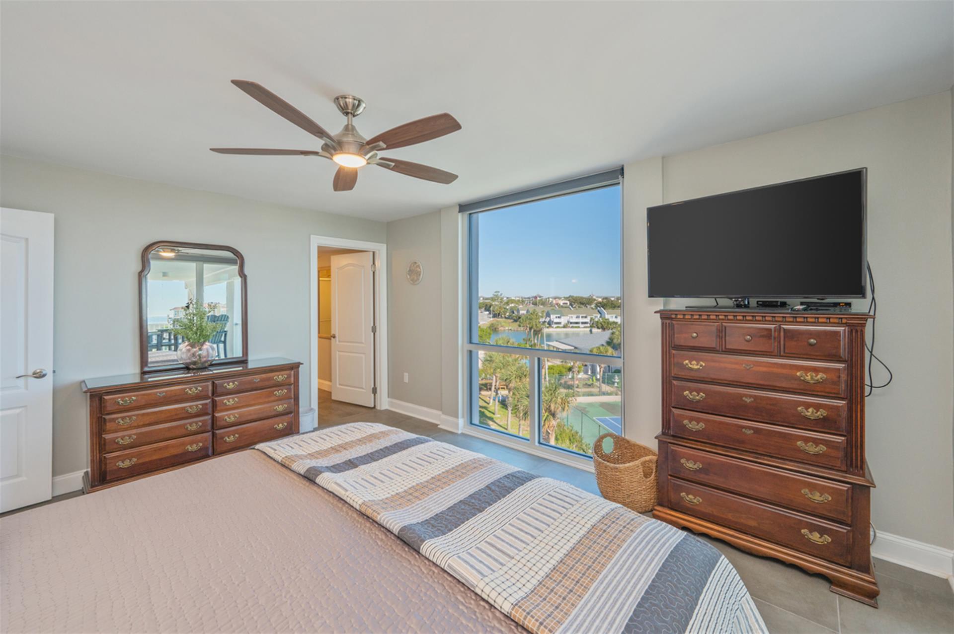 Your peaceful bedroom features rich wood furniture and a ceiling fan, with stunning views through floor-to-ceiling windows.