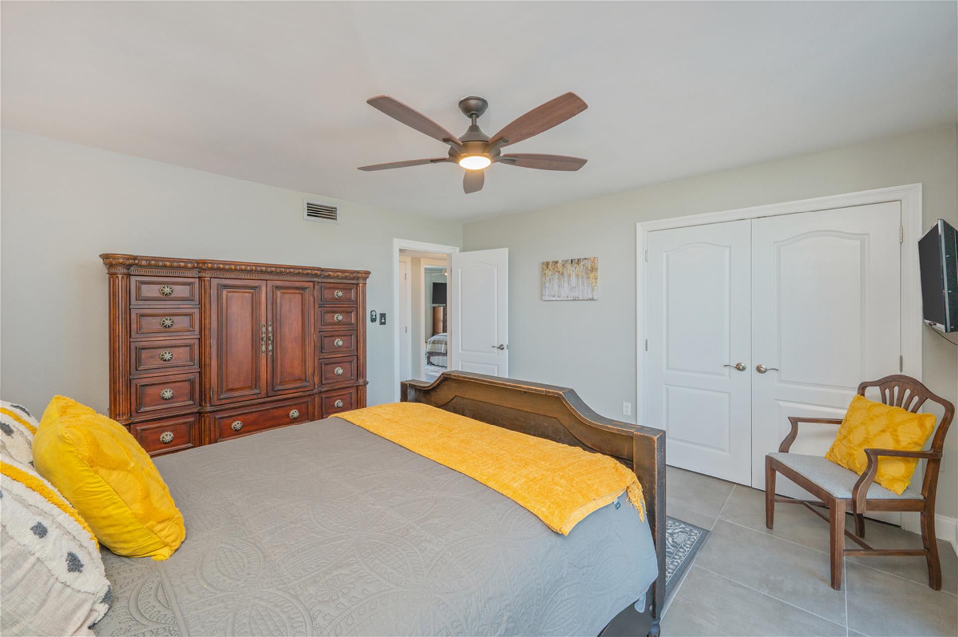 Relax in your spacious bedroom featuring a cozy bed with vibrant accents, ceiling fan for comfort, and ample storage space.