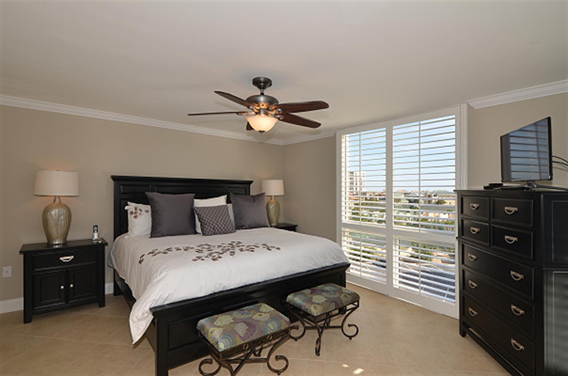 Your peaceful master bedroom features elegant dark wood furniture and large windows offering bright city views for restful mornings.