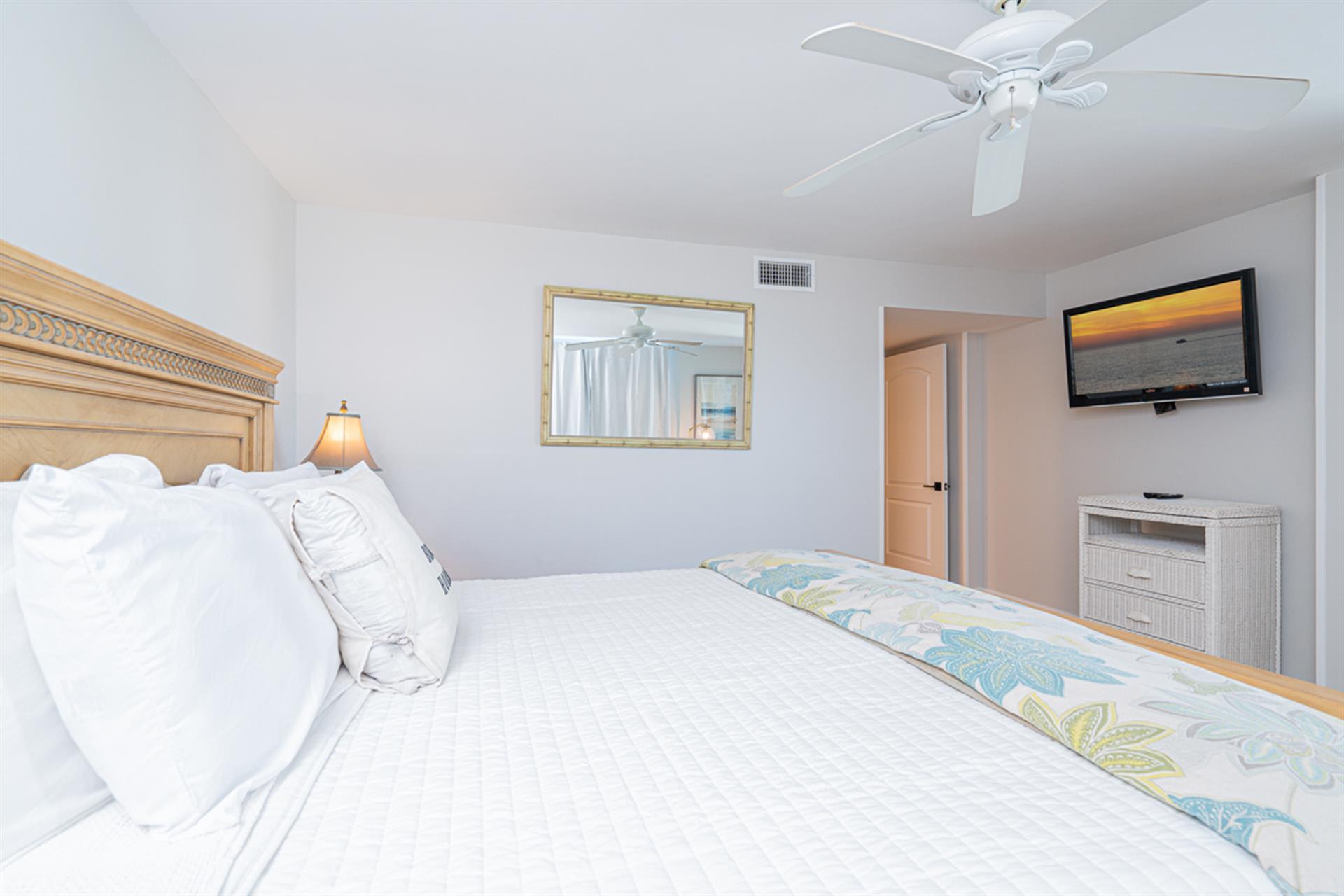 Sink into plush white linens and drift off as your ceiling fan creates a gentle breeze in this serene bedroom retreat.