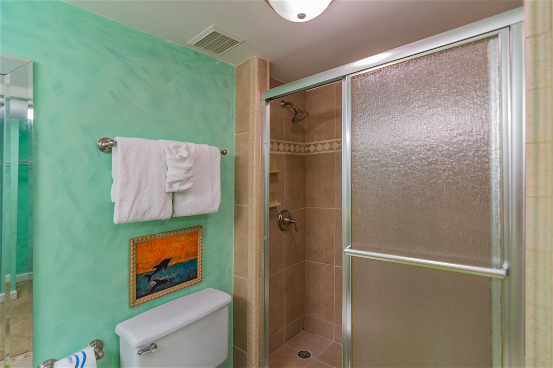 Your vibrant bathroom features calming turquoise walls and a spacious walk-in shower with elegant tiled walls, perfect for refreshing after beach days.