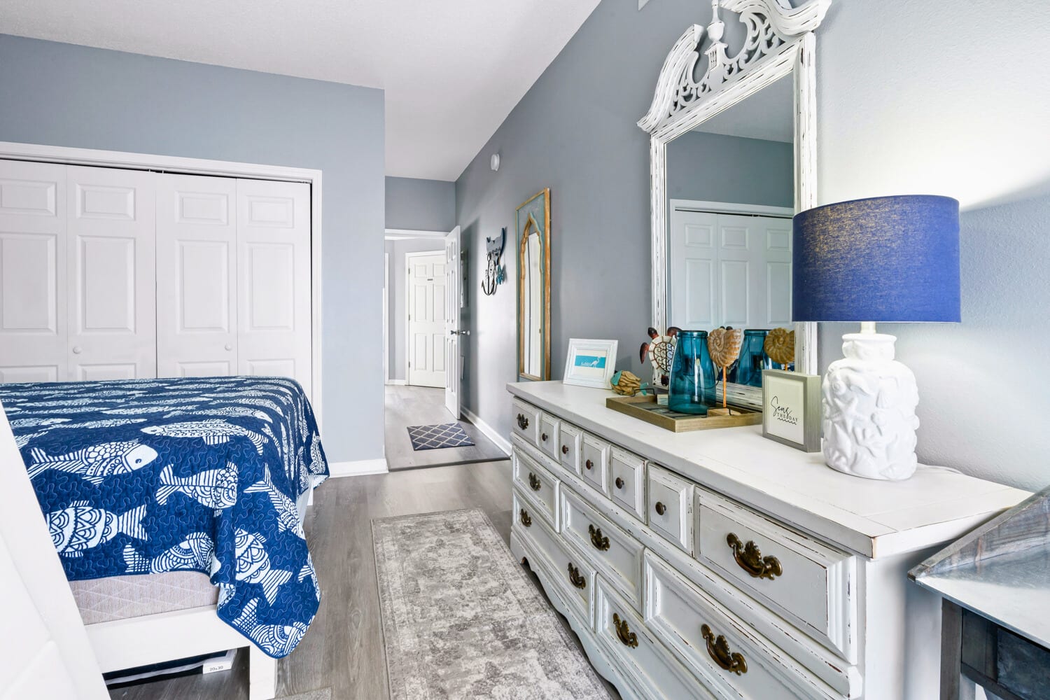 Your serene bedroom features soothing blue walls, elegant white furniture, and thoughtful coastal touches that create the perfect retreat for relaxation.