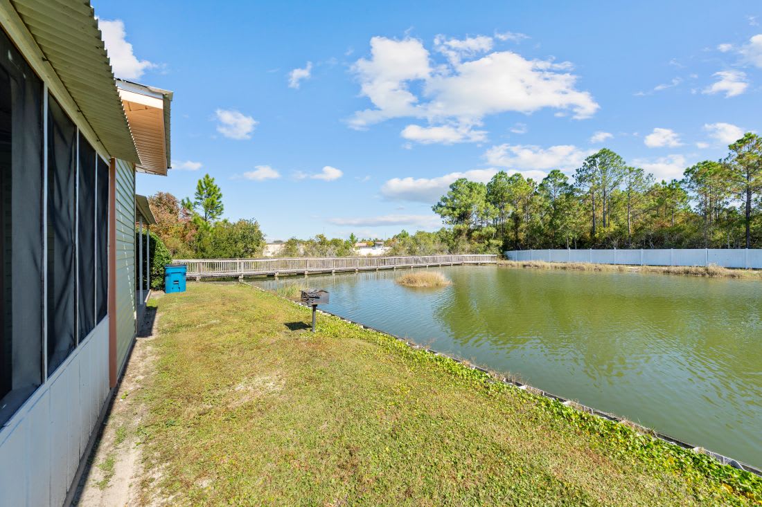 Waterfront property featuring a peaceful lake with walking bridge and lush natural surroundings under bright blue skies.
