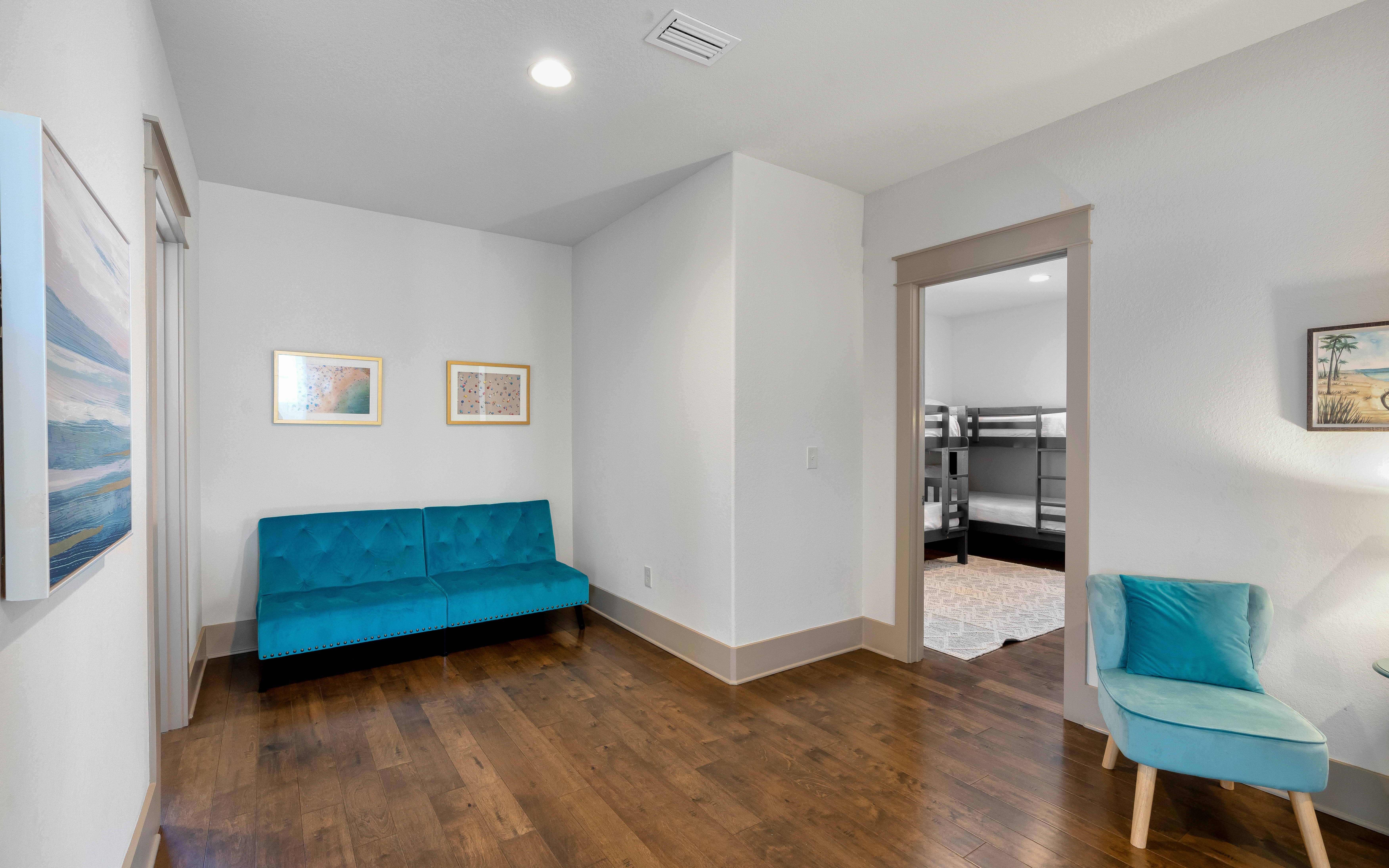 Unwind in your bright living space featuring rich hardwood floors and stylish teal seating that invites relaxation.