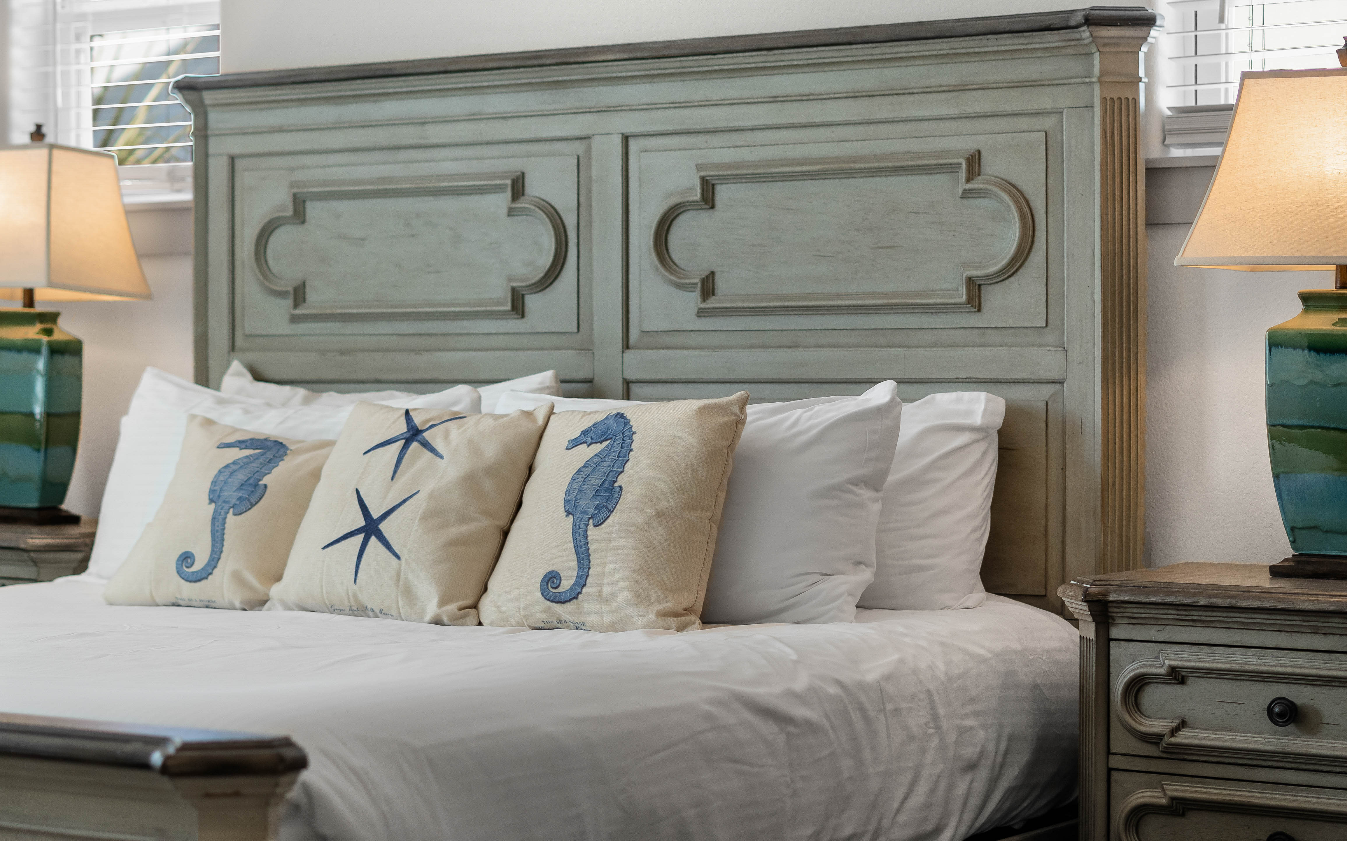 Drift into coastal dreams on crisp white linens, surrounded by charming seahorse pillows and weathered wood furniture that whispers of ocean breezes.