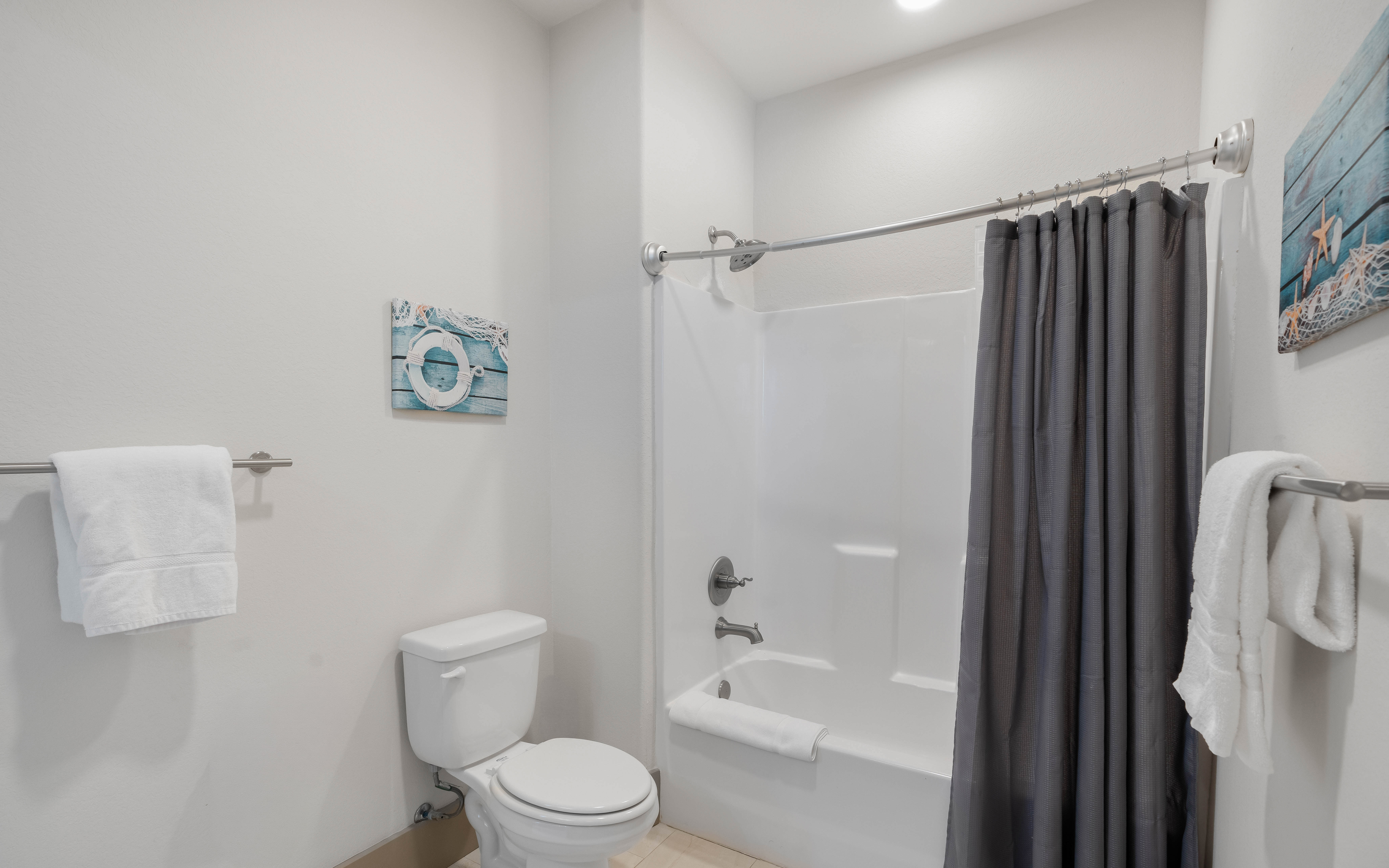 Step into your sparkling clean bathroom featuring a relaxing tub-shower combo, fresh towels, and cheerful coastal decor.
