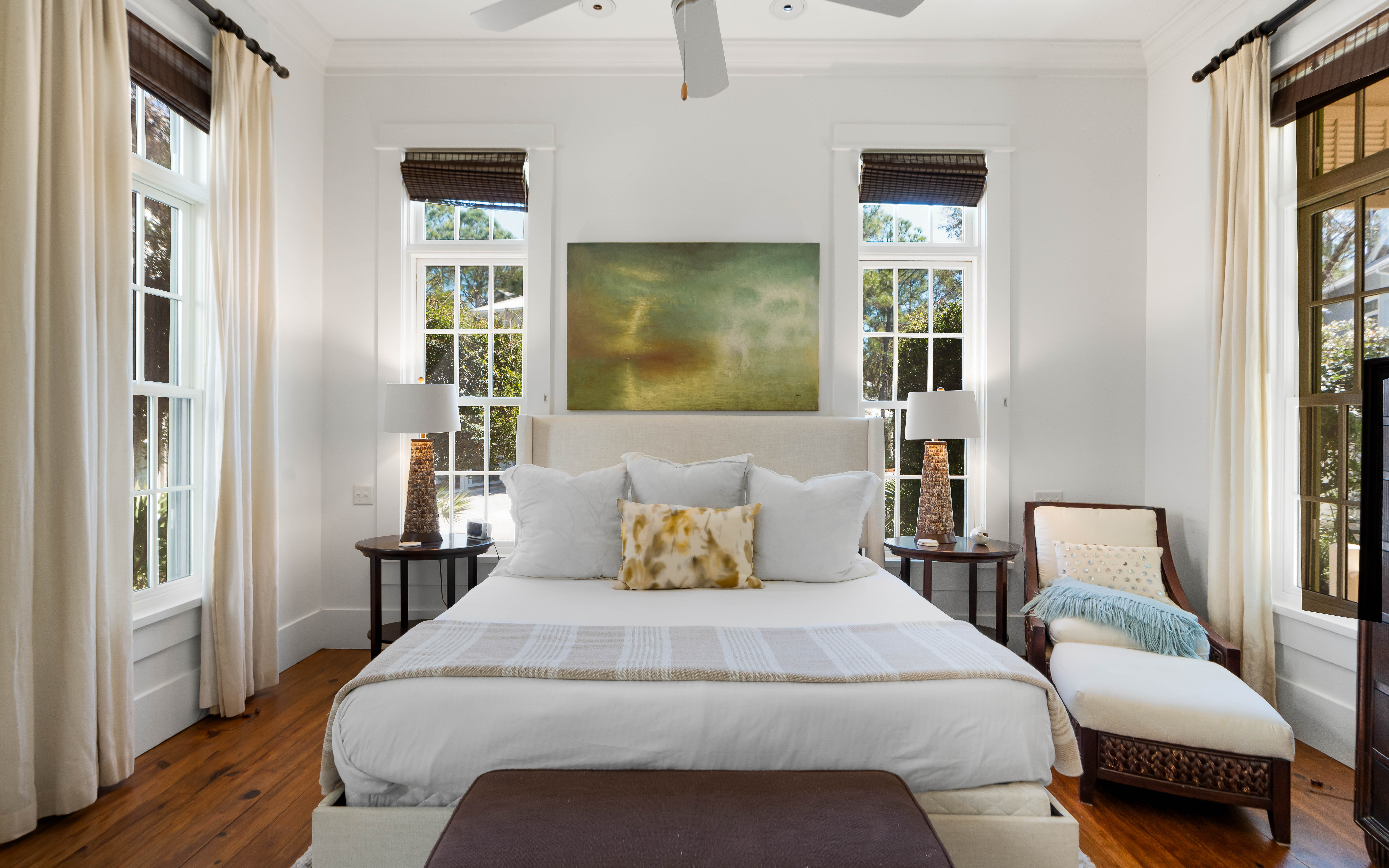 Your elegant bedroom features crisp white linens, warm hardwood floors, and natural light streaming through multiple windows for peaceful mornings.
