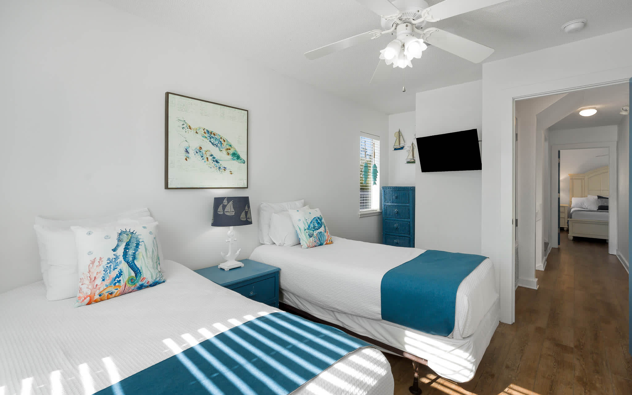 Your coastal-themed bedroom with twin beds, ocean artwork, and ceiling fan creates a refreshing retreat after beach adventures.