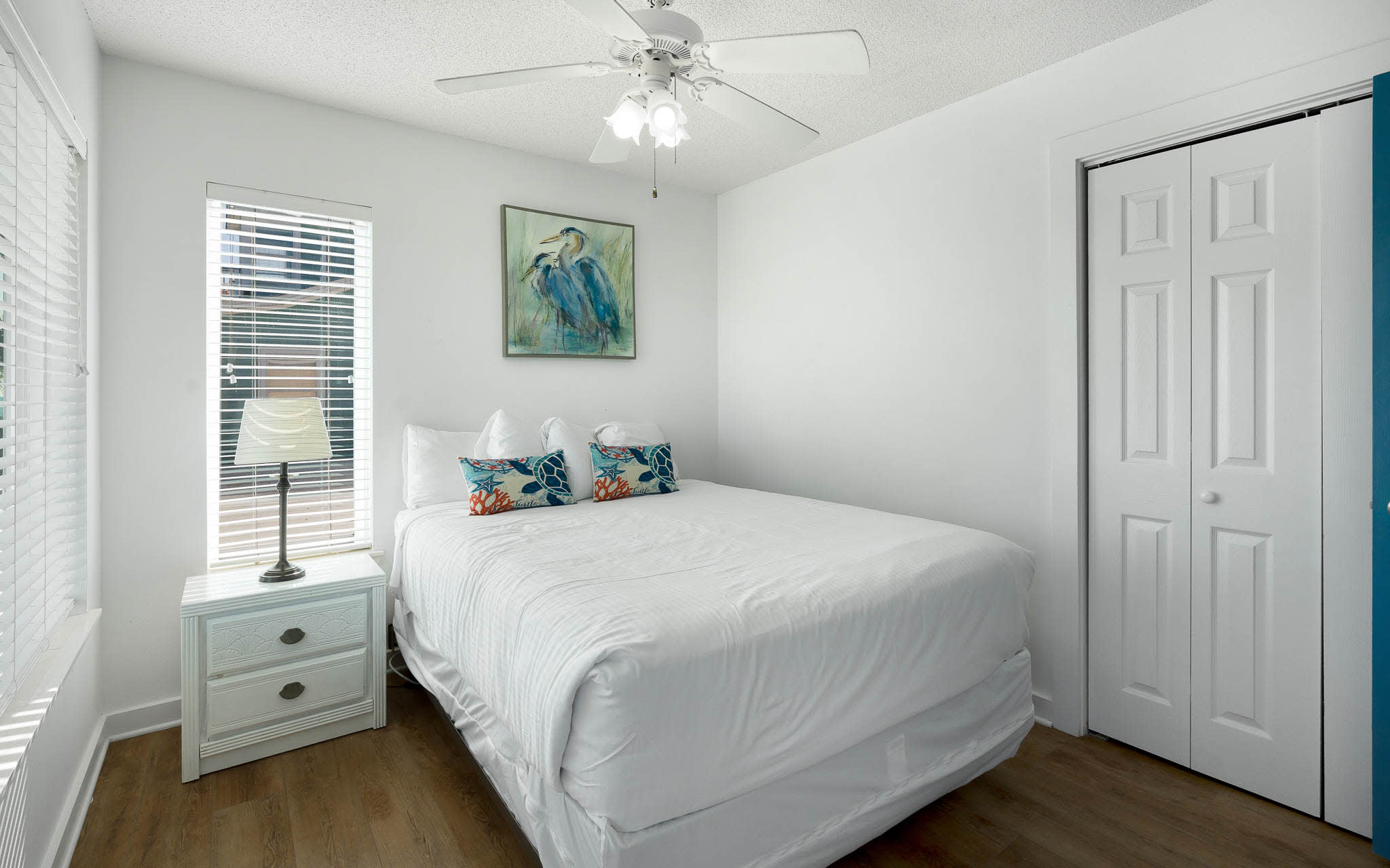 Drift into peaceful sleep in your bright bedroom, complete with fresh linens, tropical artwork, and gentle ceiling fan for perfect comfort.