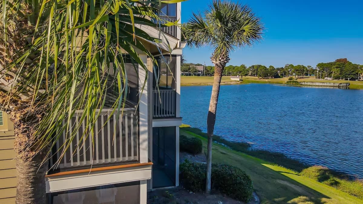 Screened balcony overlooks a peaceful lake lined with palm trees, offering the perfect spot to unwind and enjoy the serene, coastal surroundings.