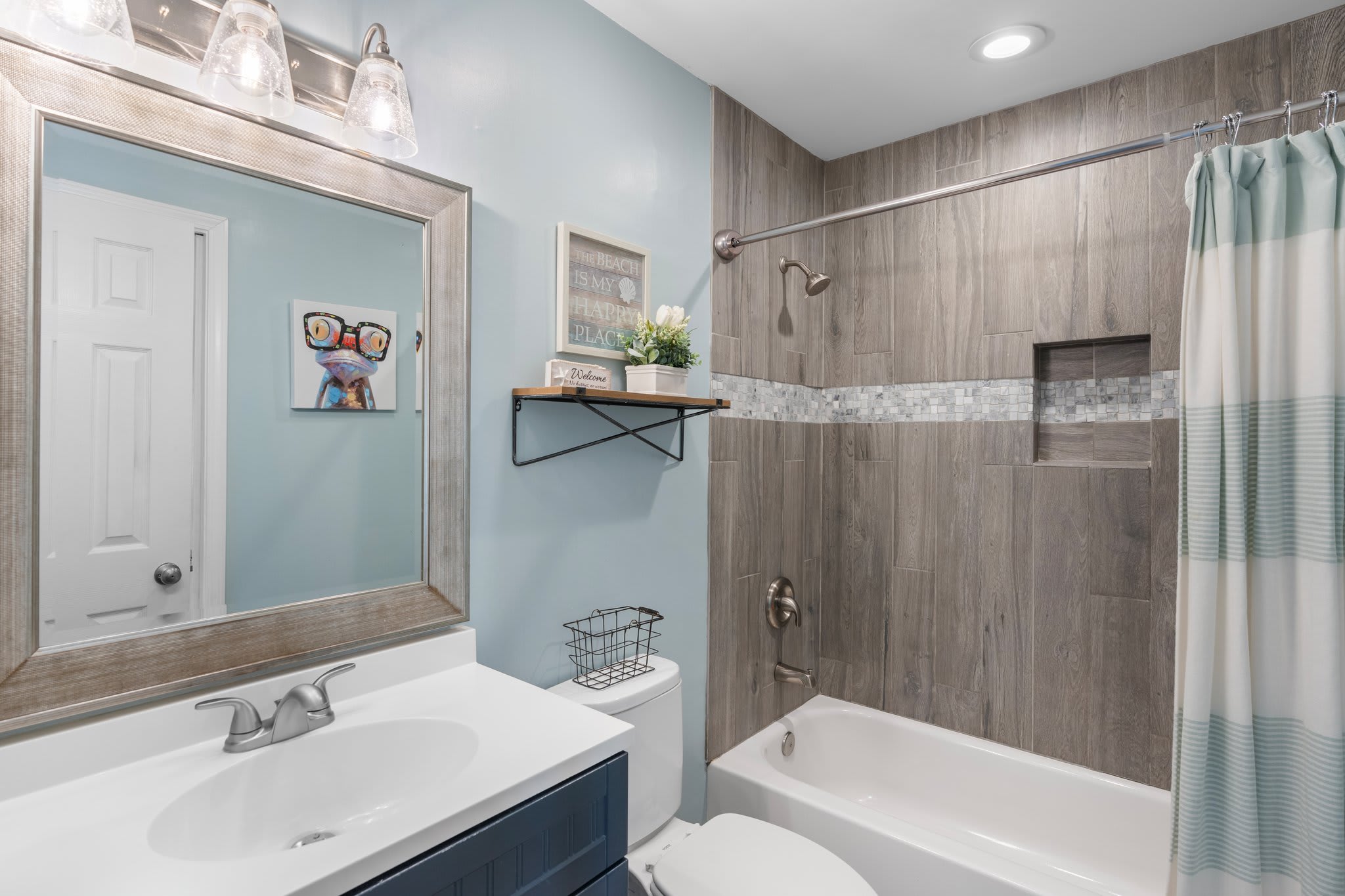 Stylish guest bathroom with a modern vanity, upgraded tile shower, mosaic accent trim, and playful coastal decor—perfect blend of comfort and charm.