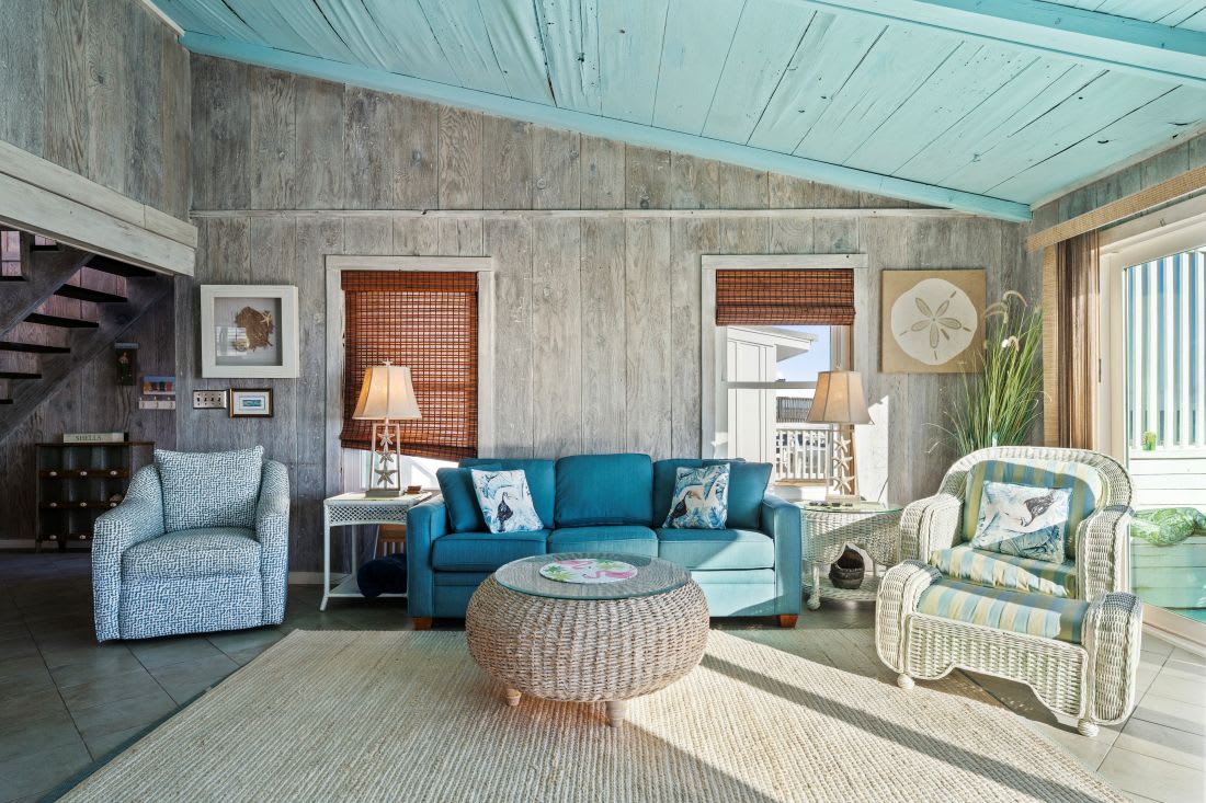 Relax in this coastal living room with turquoise ceiling, ocean-blue sofa, and wicker furnishings that perfectly capture beachside charm.