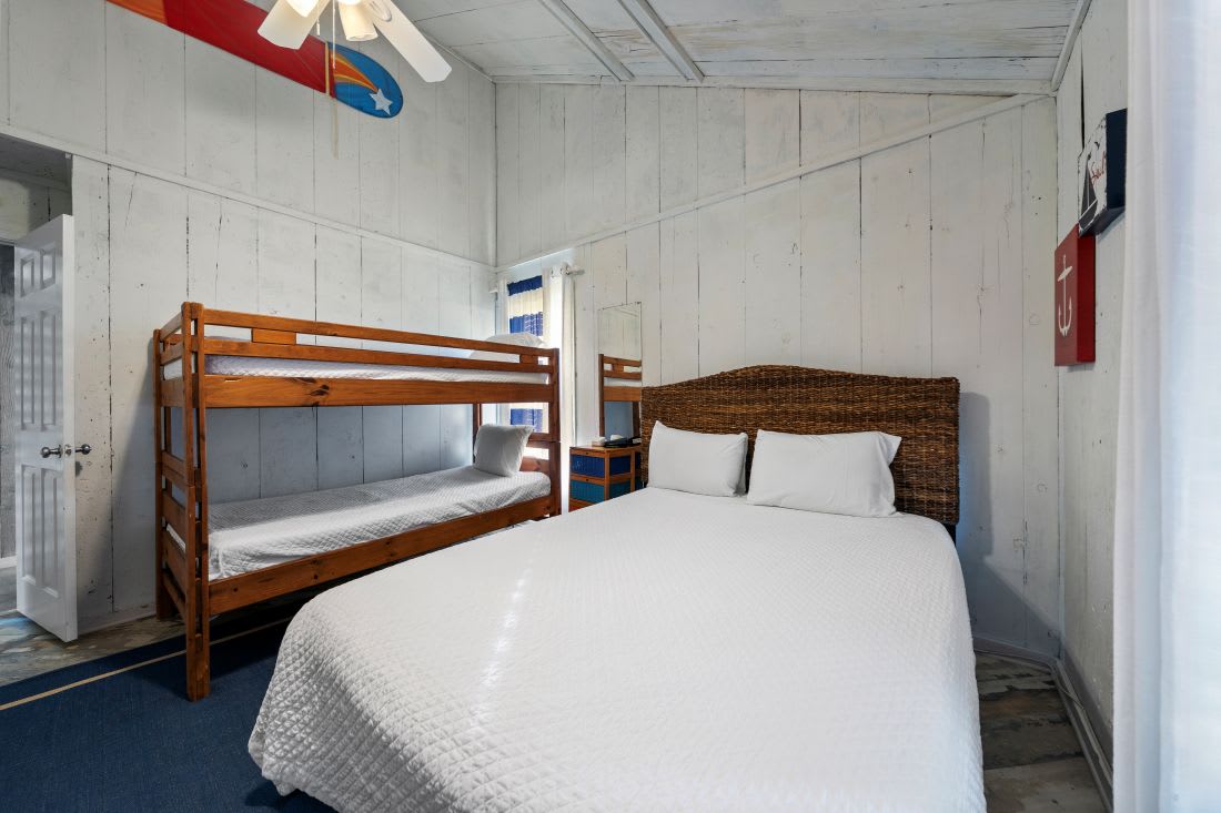 Cozy coastal bedroom with queen bed and bunk beds, perfect for families seeking comfort and fun.