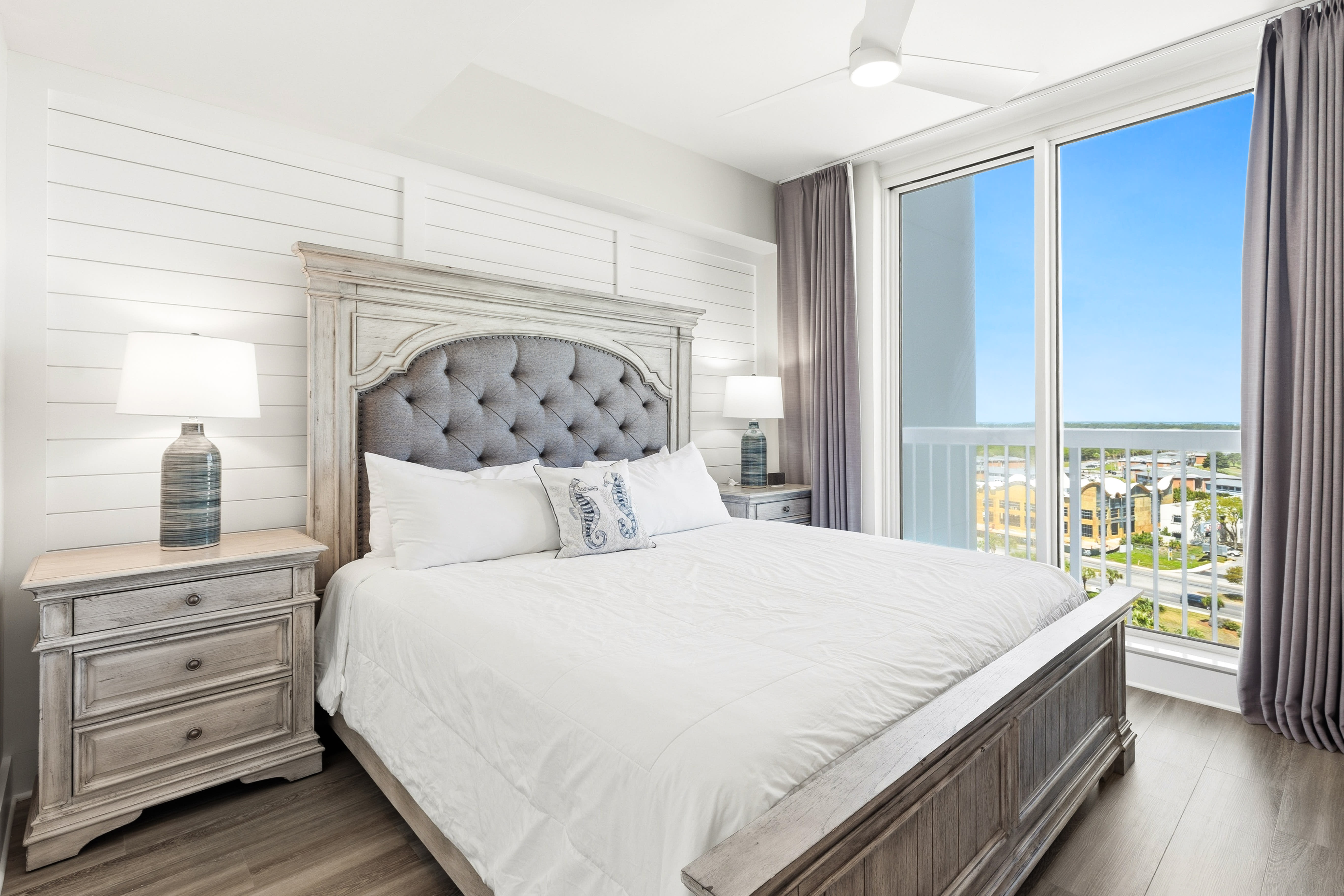 Drift off in your elegant bedroom featuring a plush tufted headboard, crisp white linens, and sweeping balcony views.